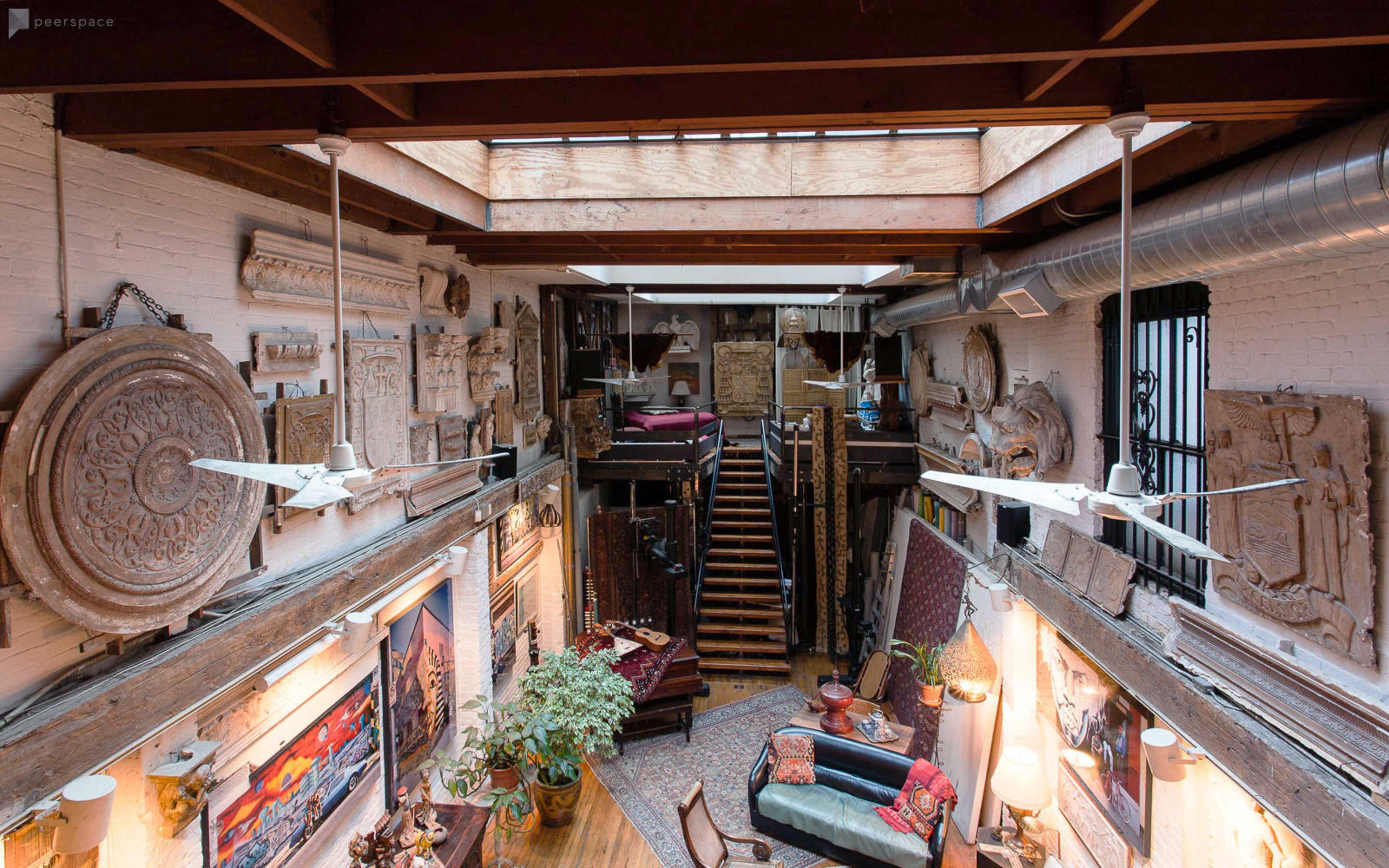 The image shows a spacious loft with a central staircase, featuring decorative wall art and large skylights that allow natural light to fill the room.