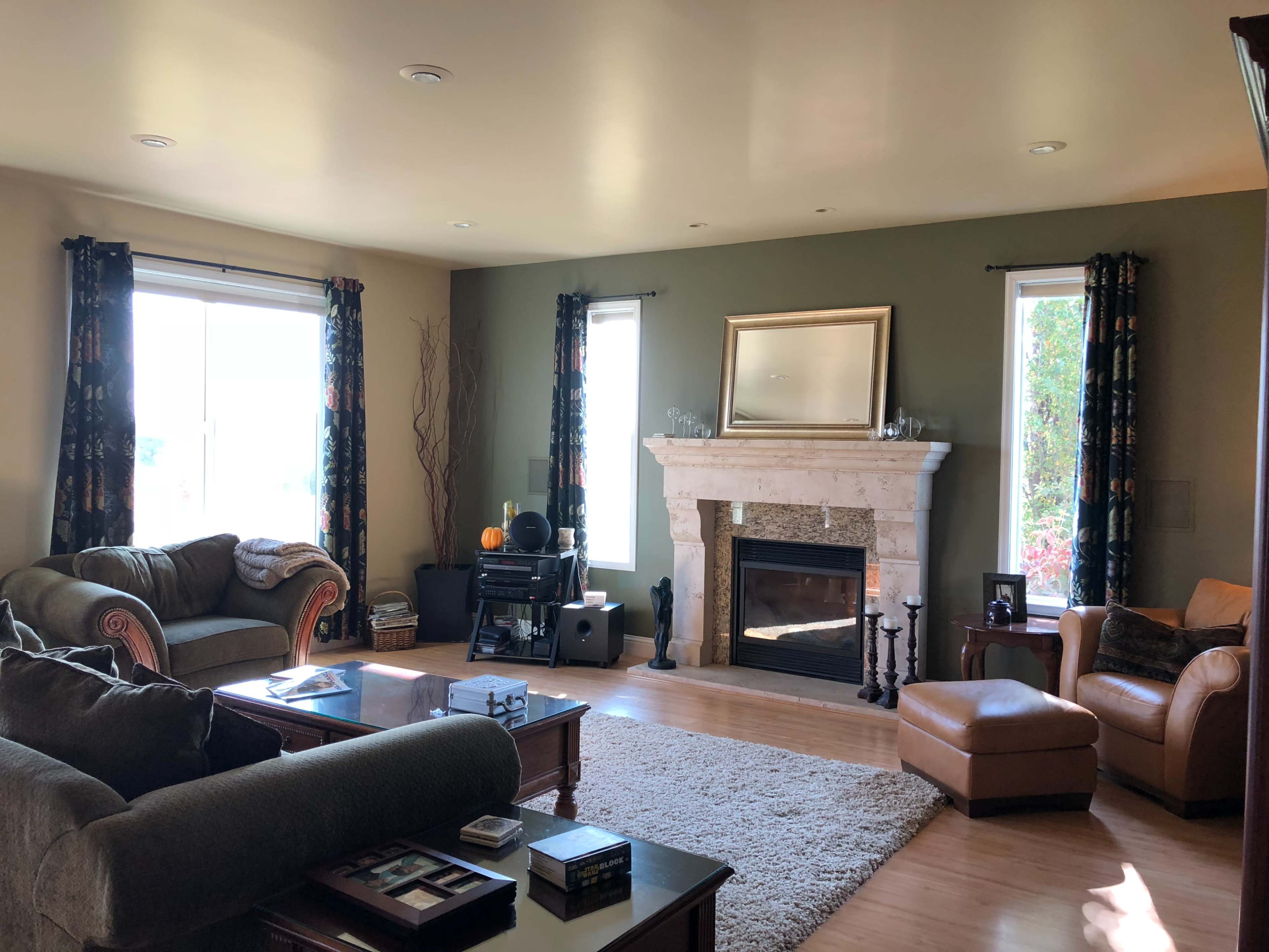 The image shows a living room with a stone fireplace, two windows, and seating arrangements consisting of a sofa and an armchair.