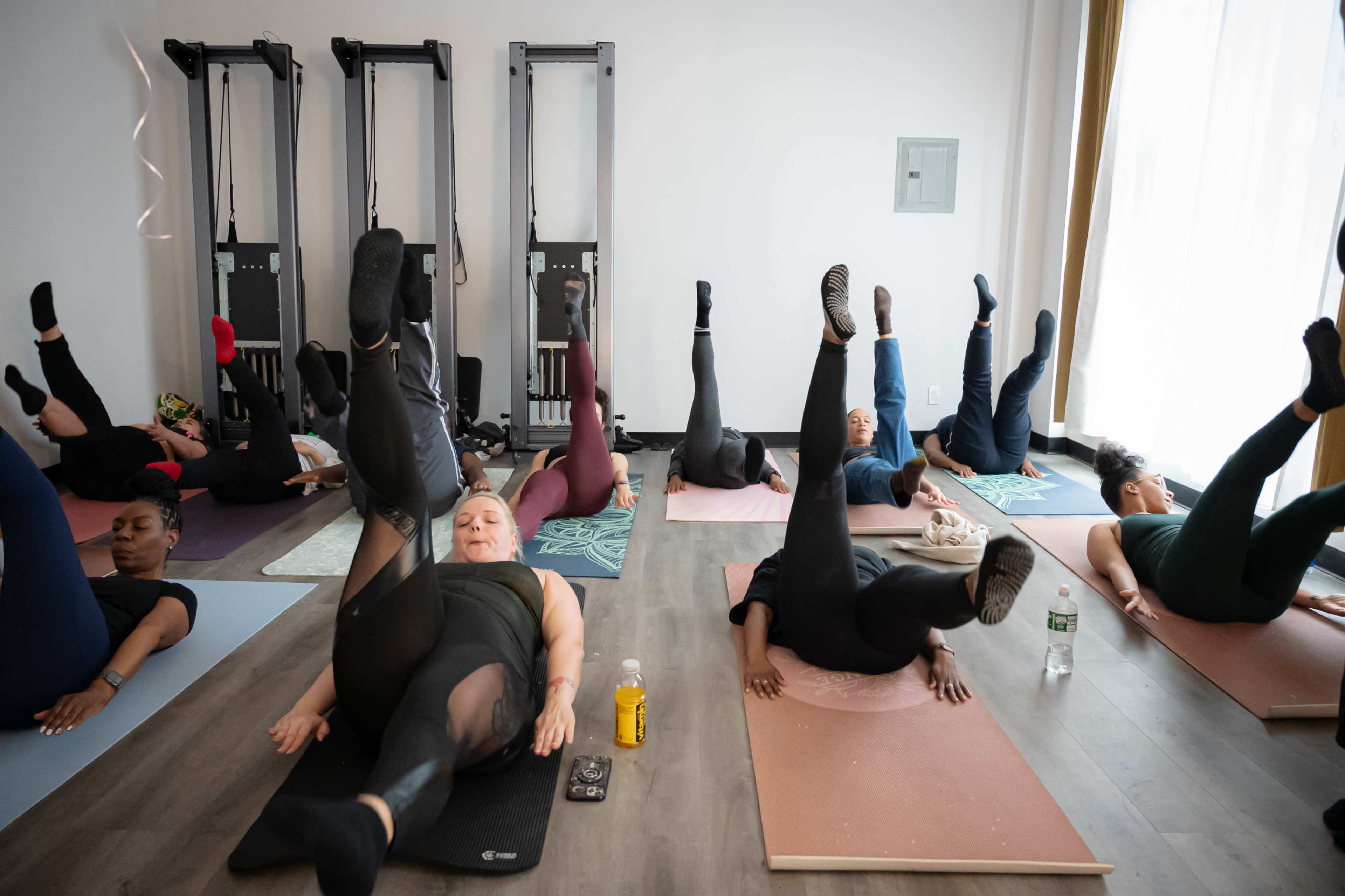 A group of individuals is participating in a fitness class on yoga mats, performing leg exercises in a brightly lit studio.