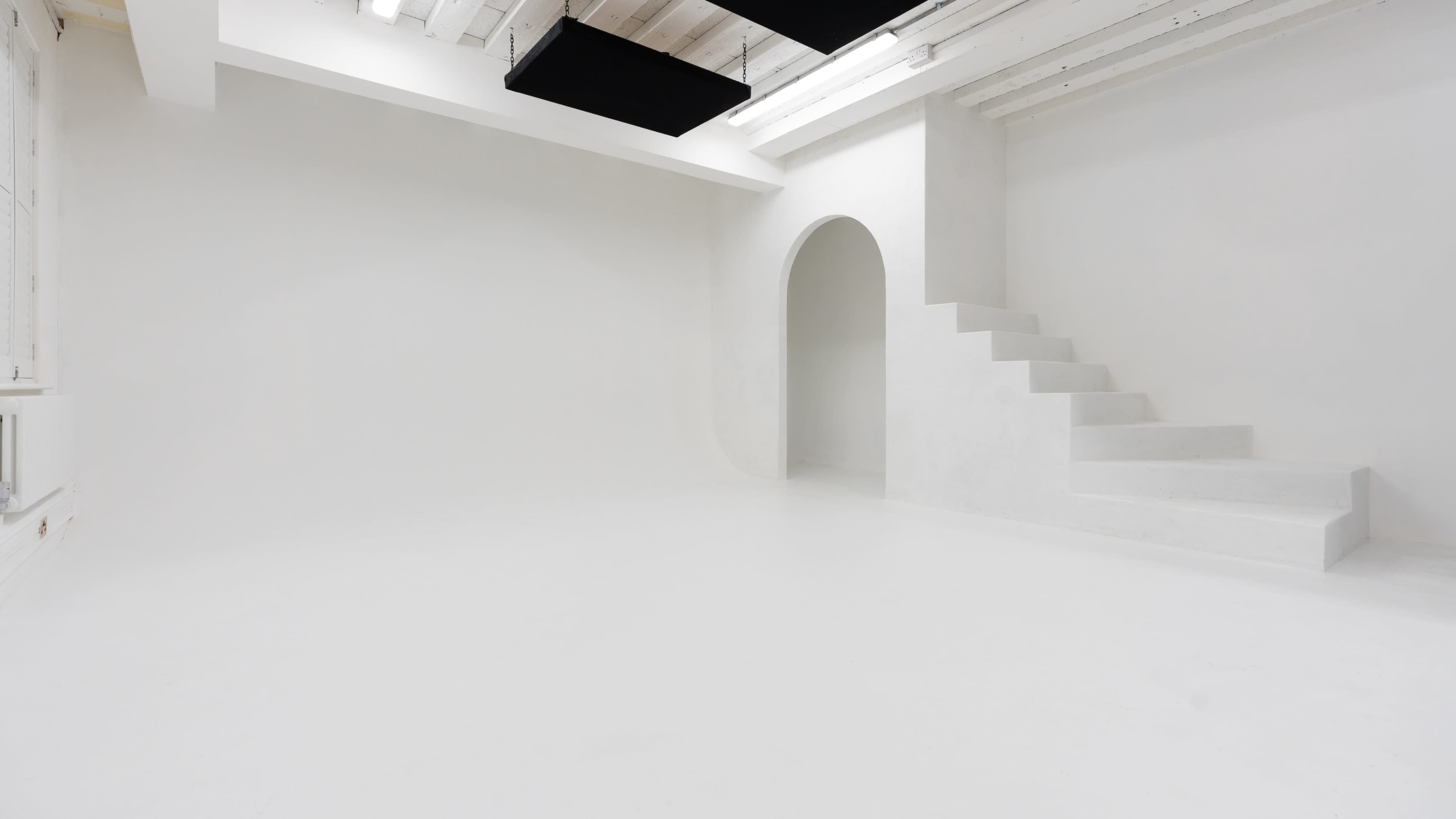 The image shows a minimalistic white room featuring a staircase leading to an archway.