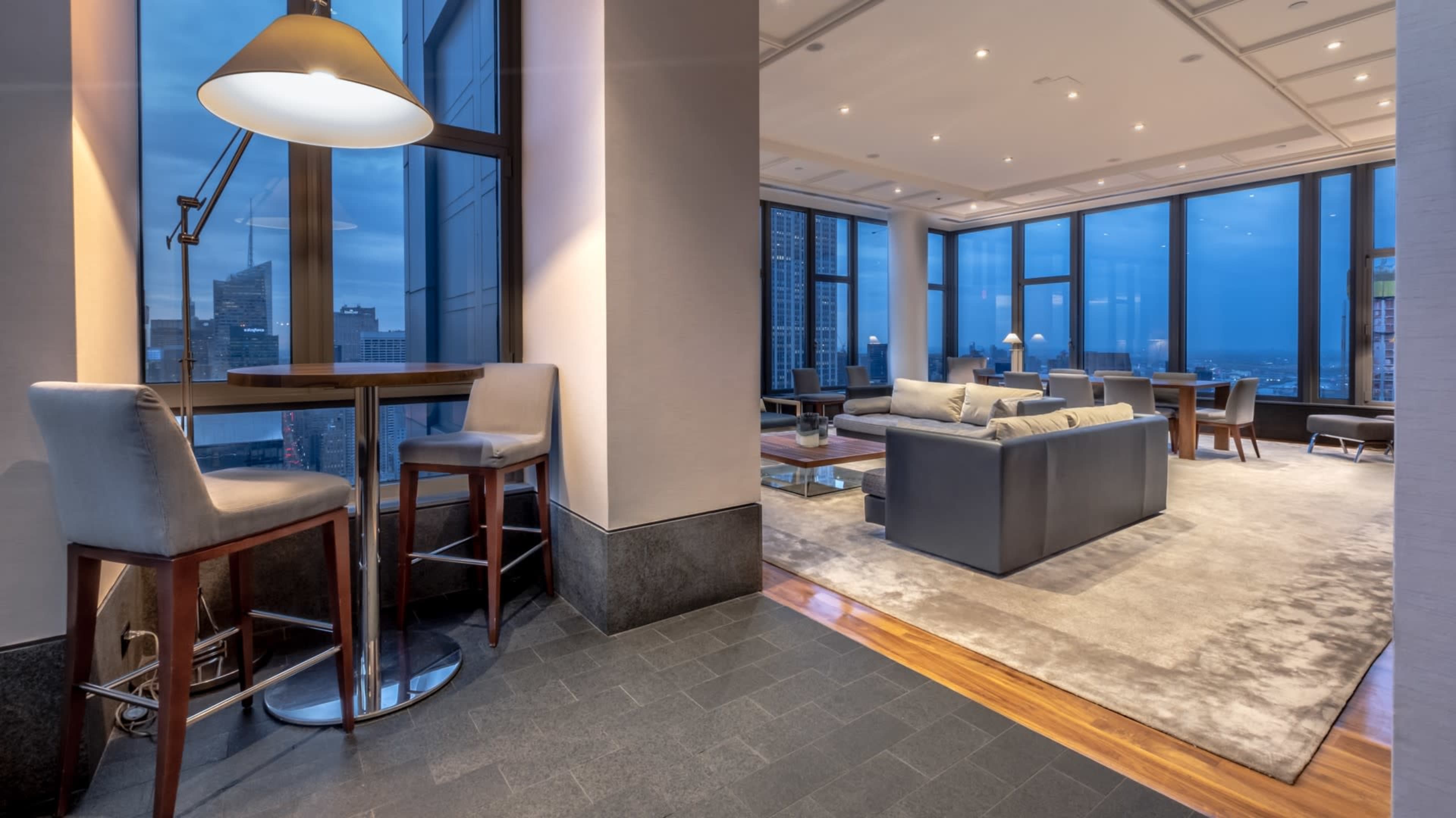 A modern lounge area with large windows, contemporary furniture, and a bar-style seating arrangement.