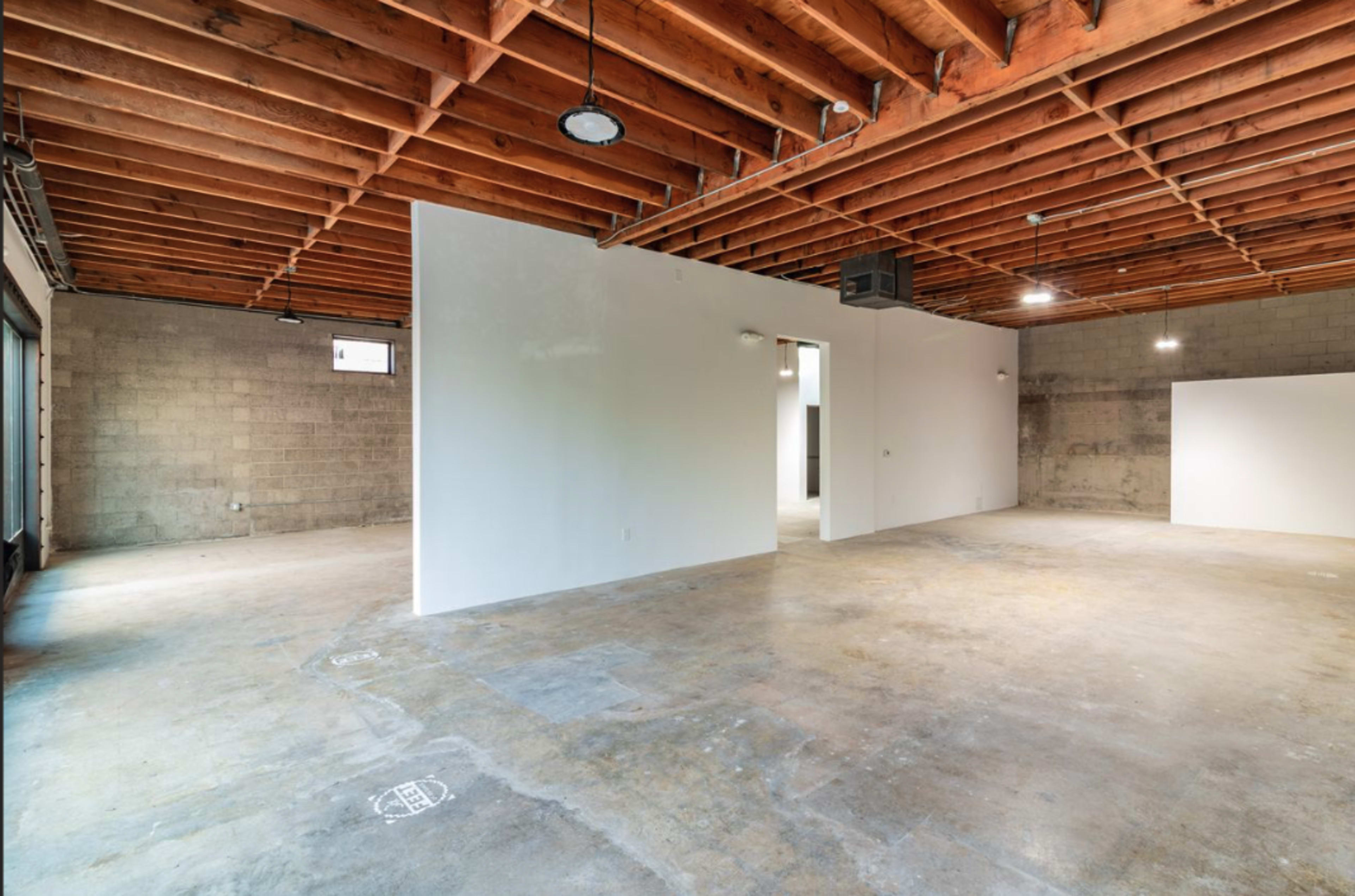 The image shows an empty room with exposed wooden beams and grey concrete walls and flooring.