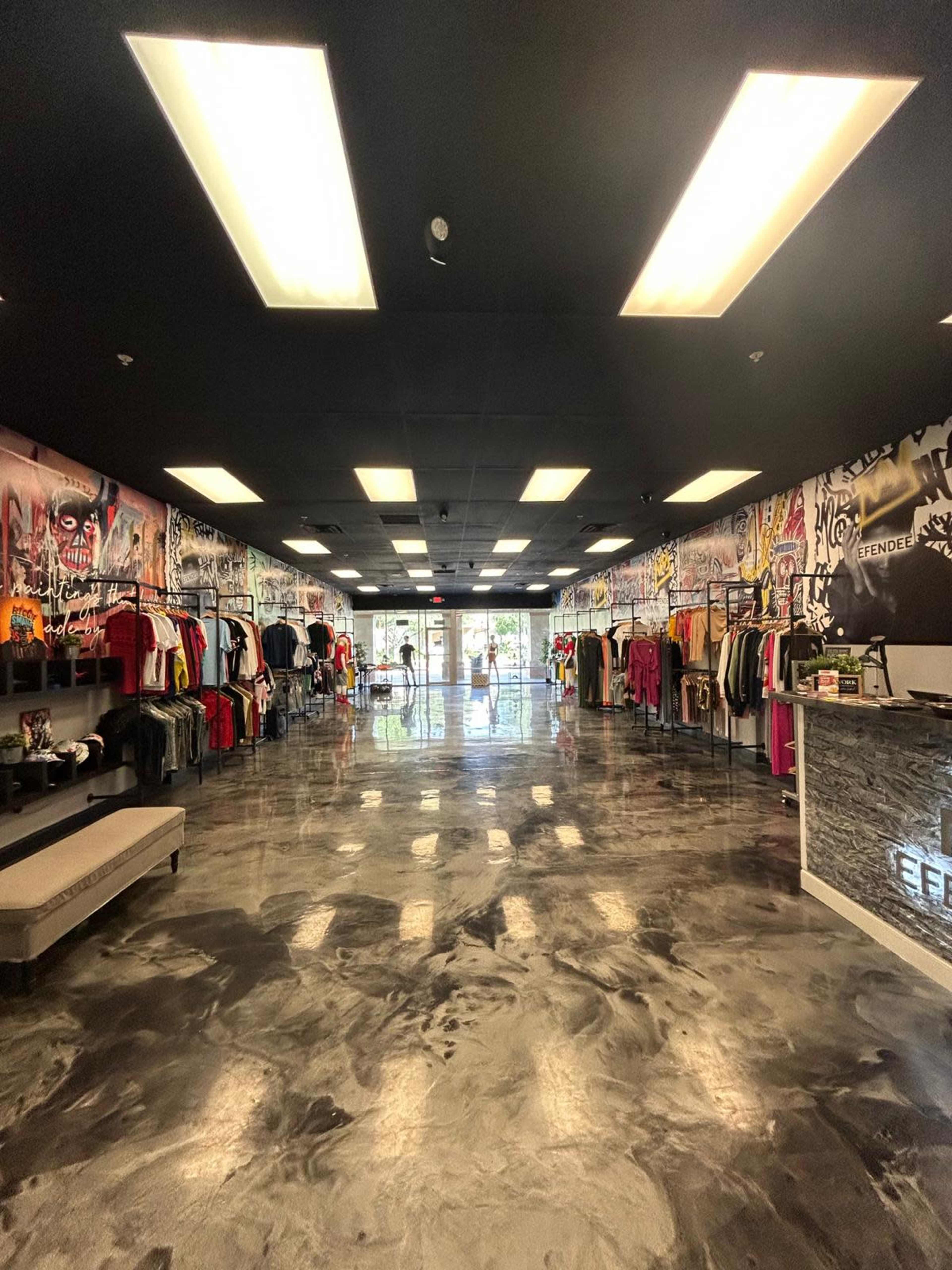 The image shows the interior of a clothing store featuring a polished concrete floor and walls adorned with graffiti-style art, with clothing racks on either side and a reception area at the front.