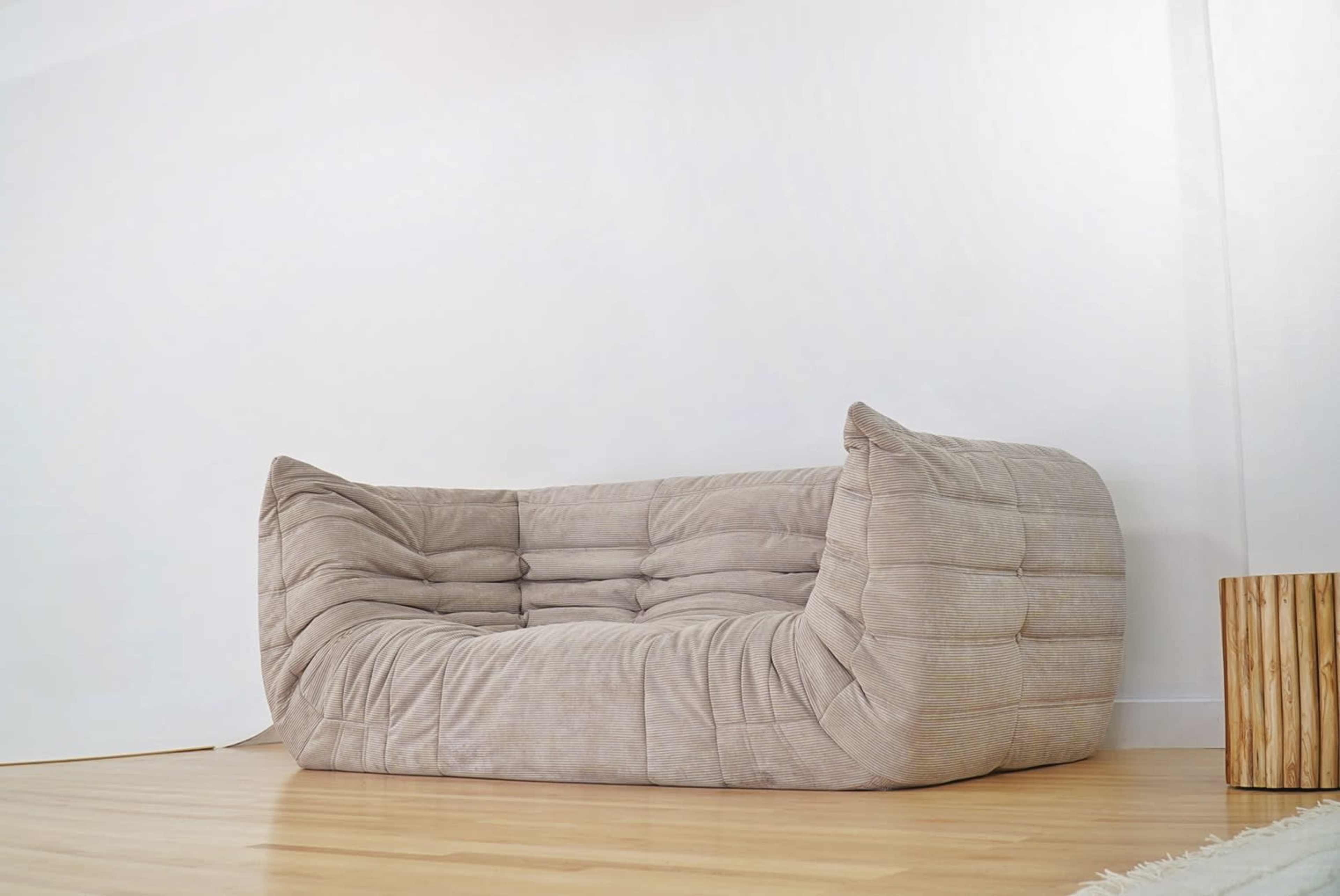 A modern, oversized beige sofa with a unique, wavy design is placed against a white wall on a wooden floor.