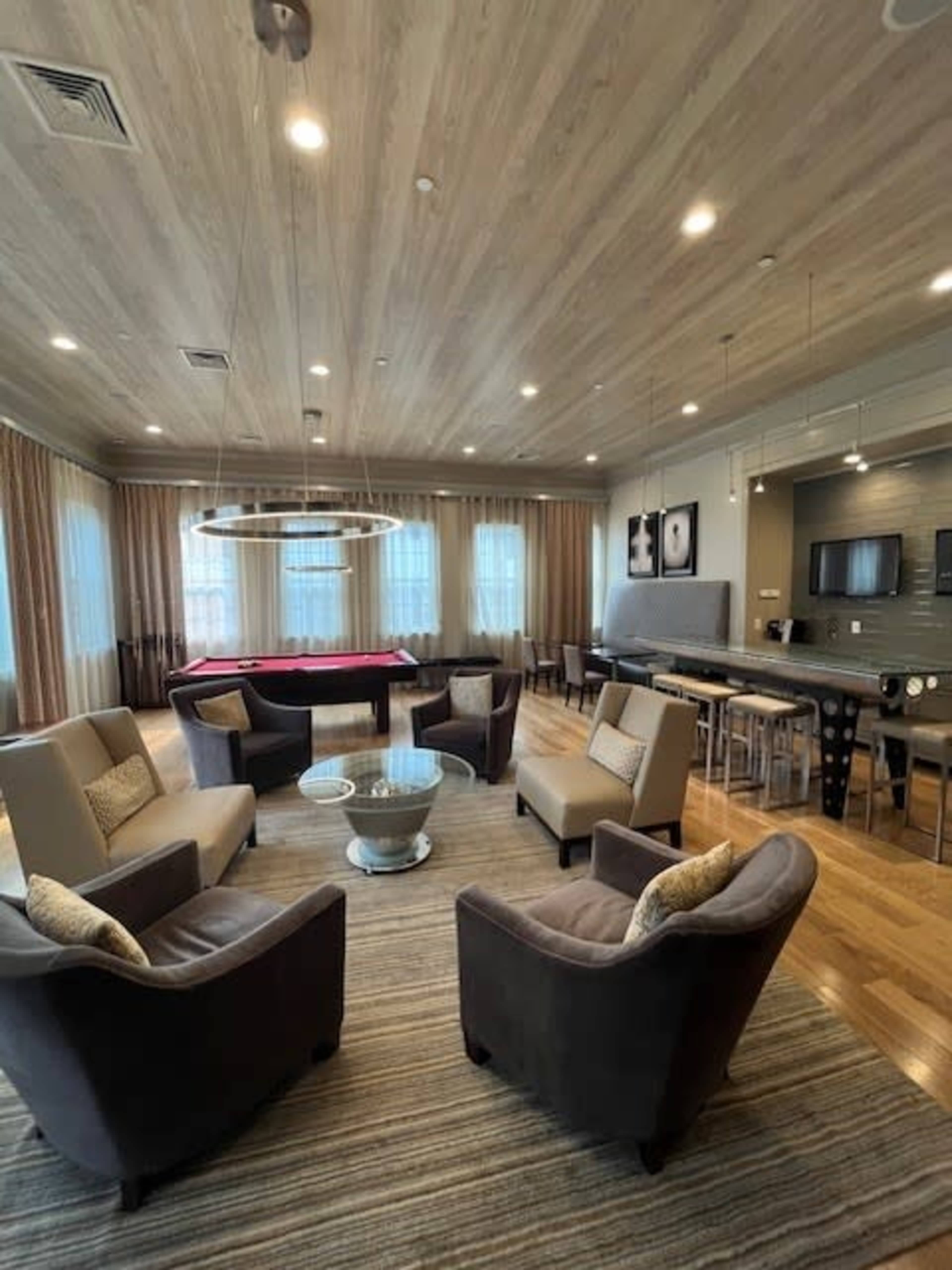 A spacious lounge area features four armchairs arranged around a coffee table, with a pool table and dining area in the background.
