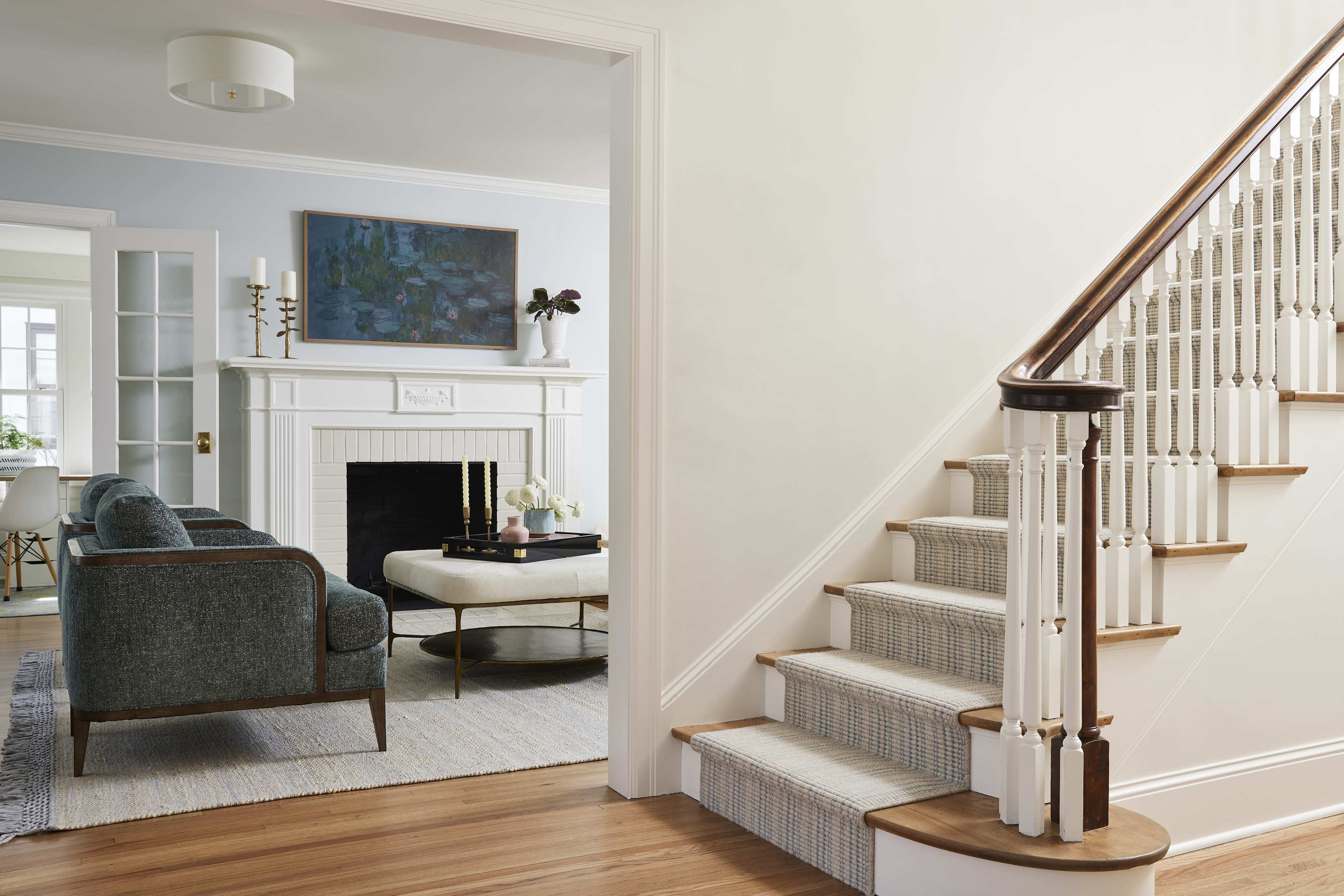 A well-lit entryway features a staircase leading to a cozy living area with a fireplace, armchairs, and a coffee table.