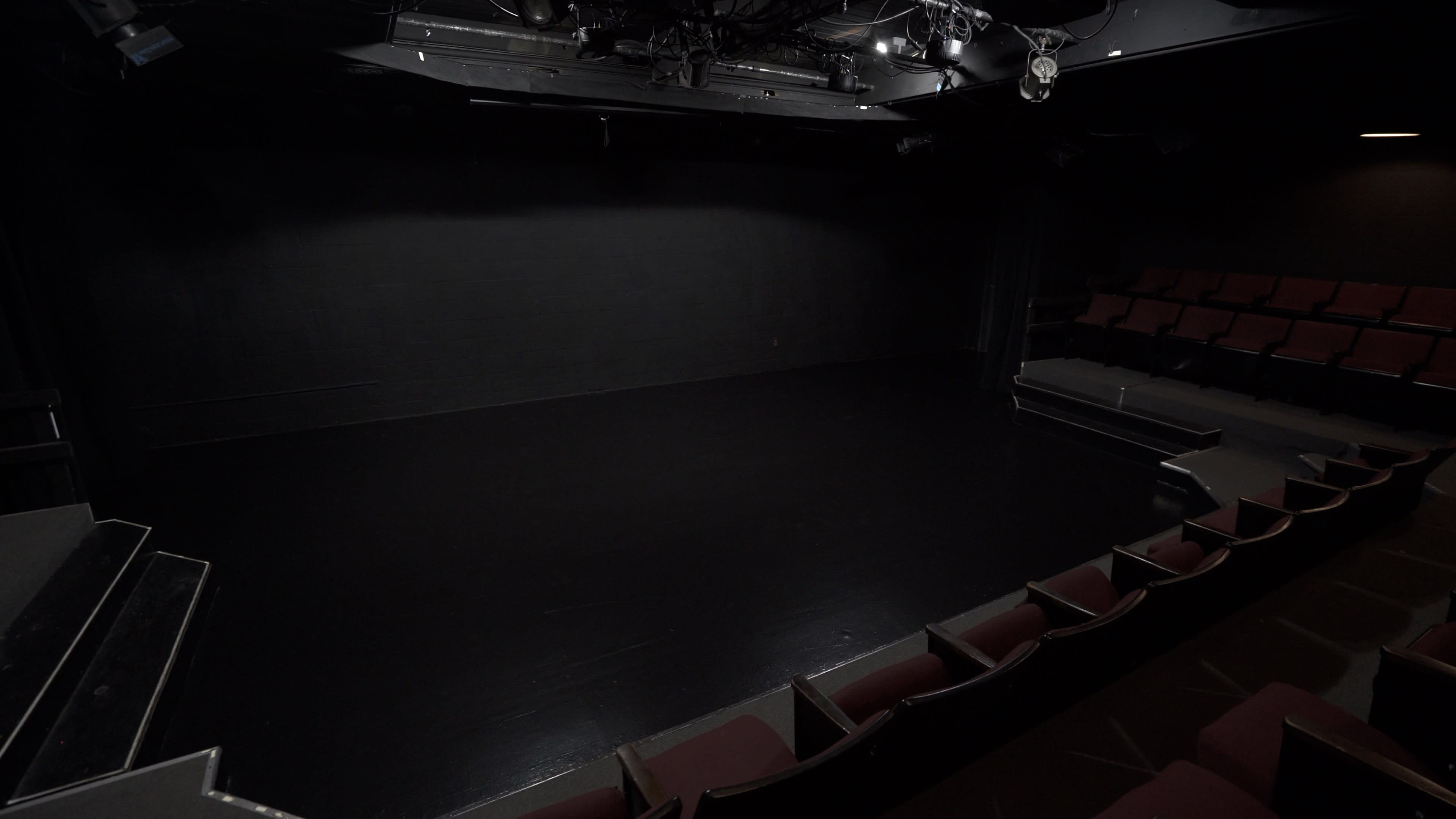 A dark theater stage with empty red seats arranged in front of it.