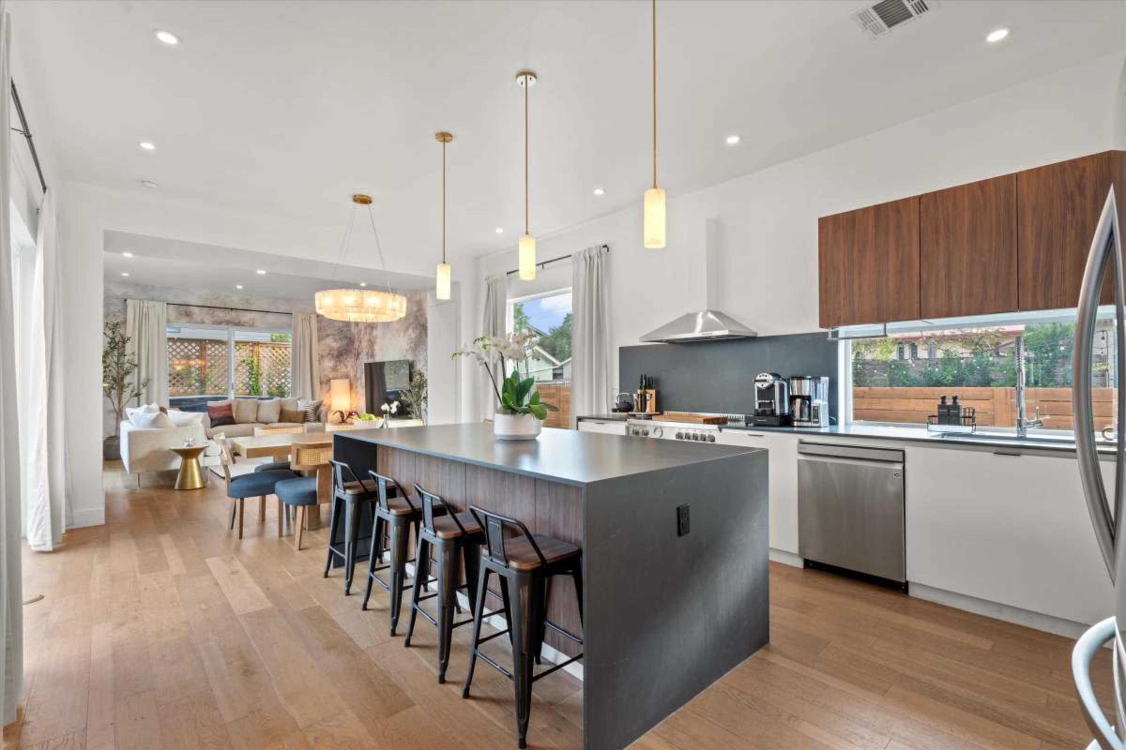 A modern kitchen features a large island with seating, sleek appliances, and a dining area that opens to a living space with natural light.