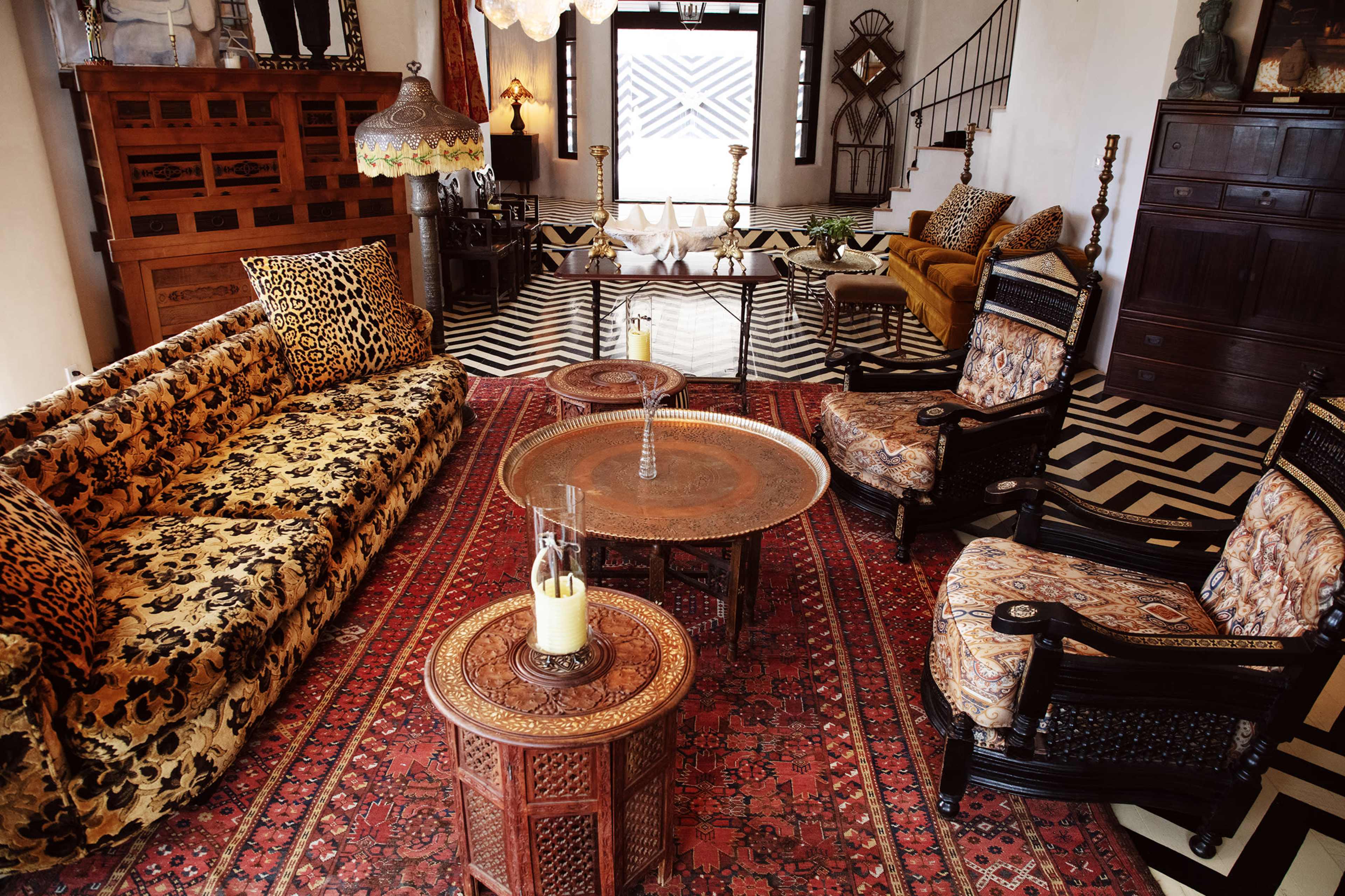 The image shows a stylish living room with patterned furniture, a decorative rug, and a mix of antique and modern decor elements.
