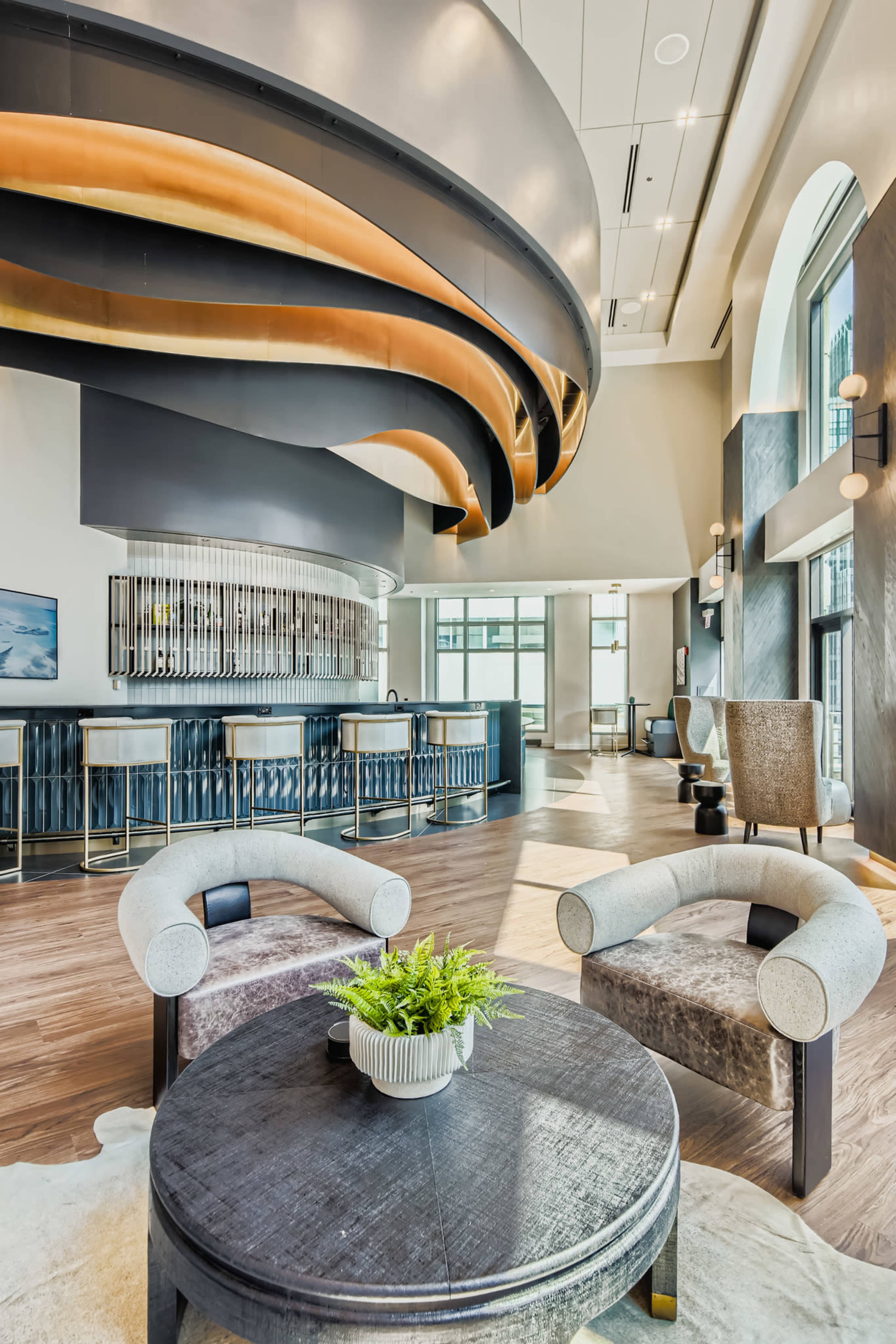 The image shows a modern interior space with a bar in the background, featuring curved architectural designs and stylish seating arrangements around a round table.
