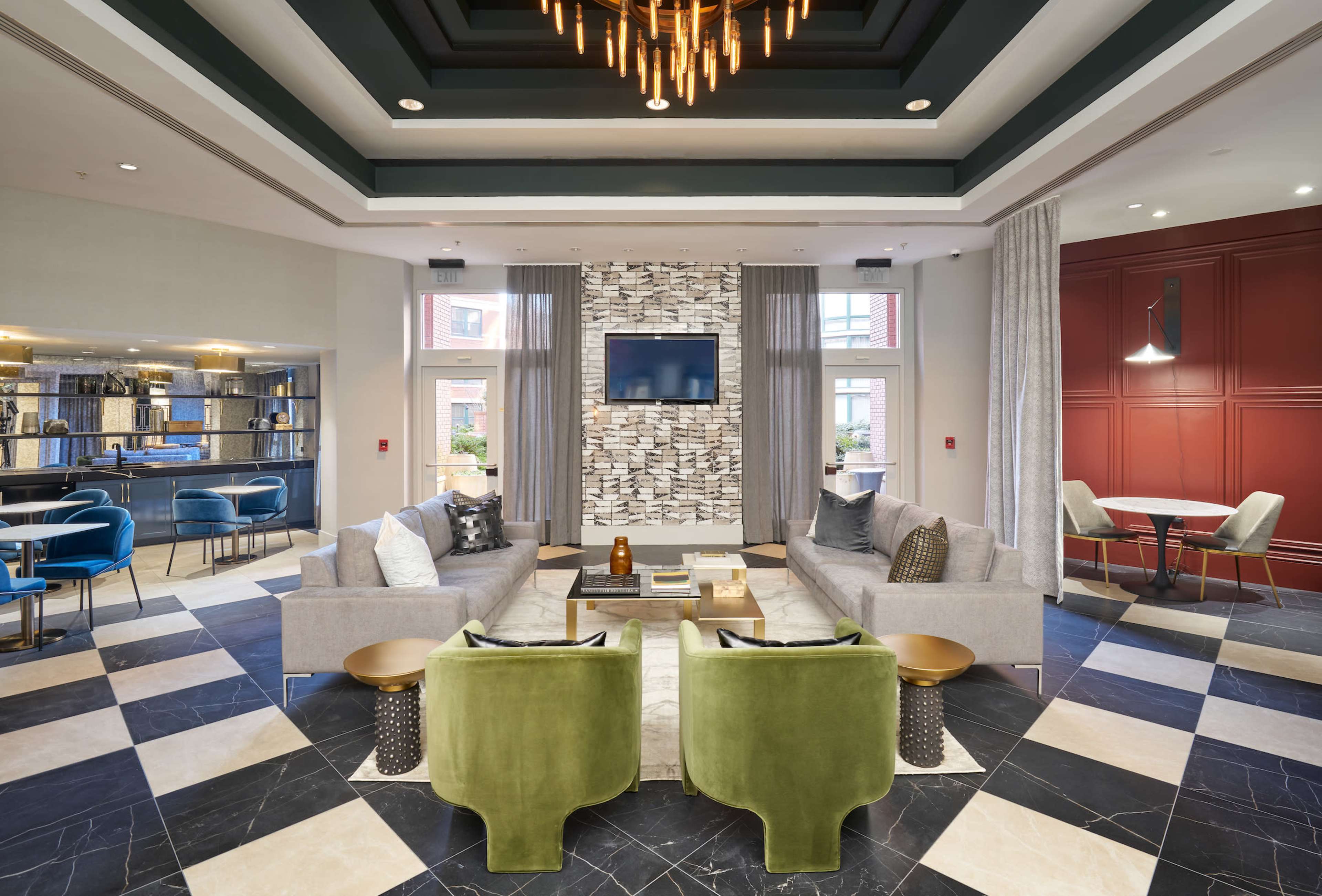 A modern lounge area featuring two green chairs, a grey sofa, a coffee table, and a light fixture hanging from the ceiling.