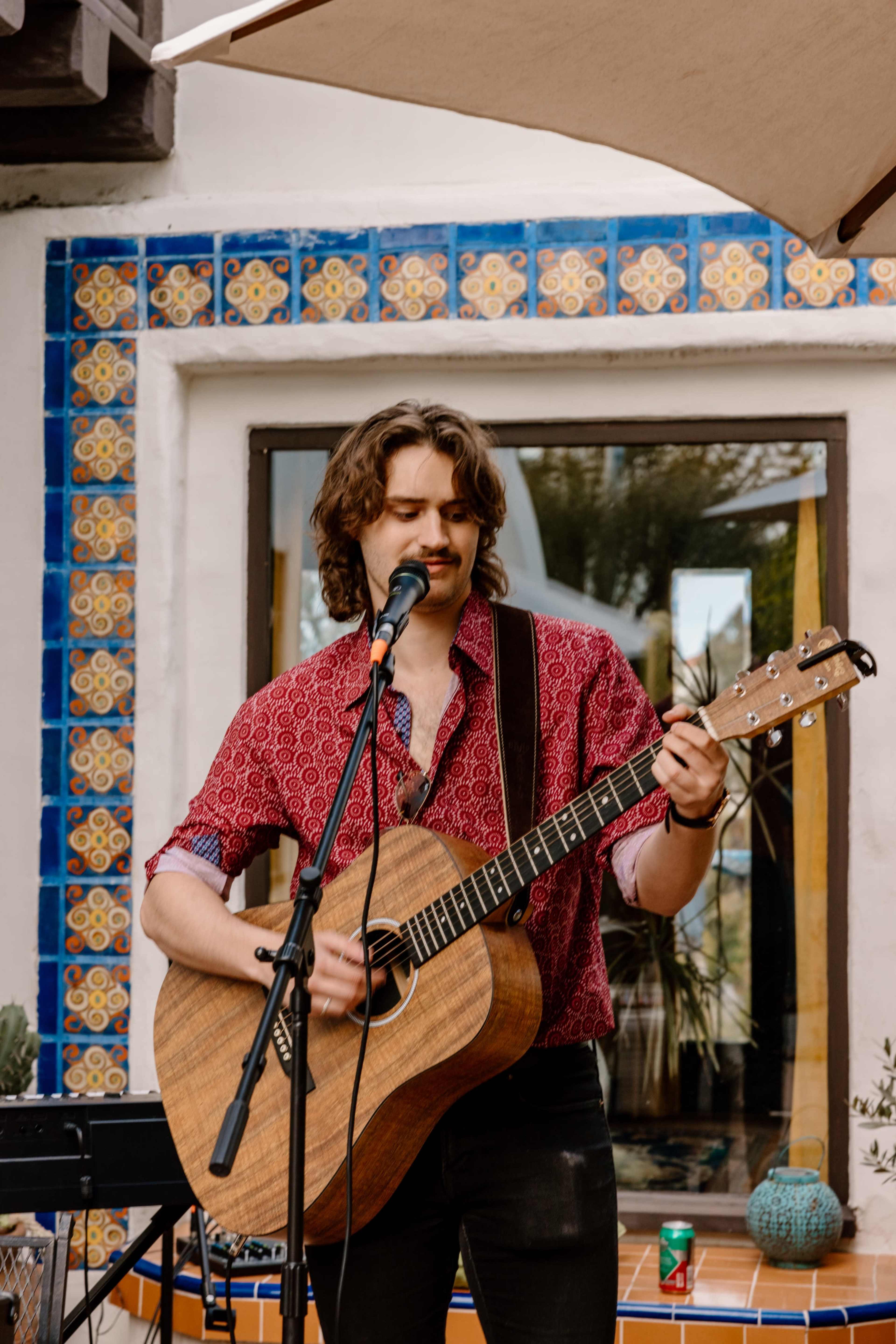 A musician performs with an acoustic guitar in an outdoor setting, surrounded by colorful tiled walls.