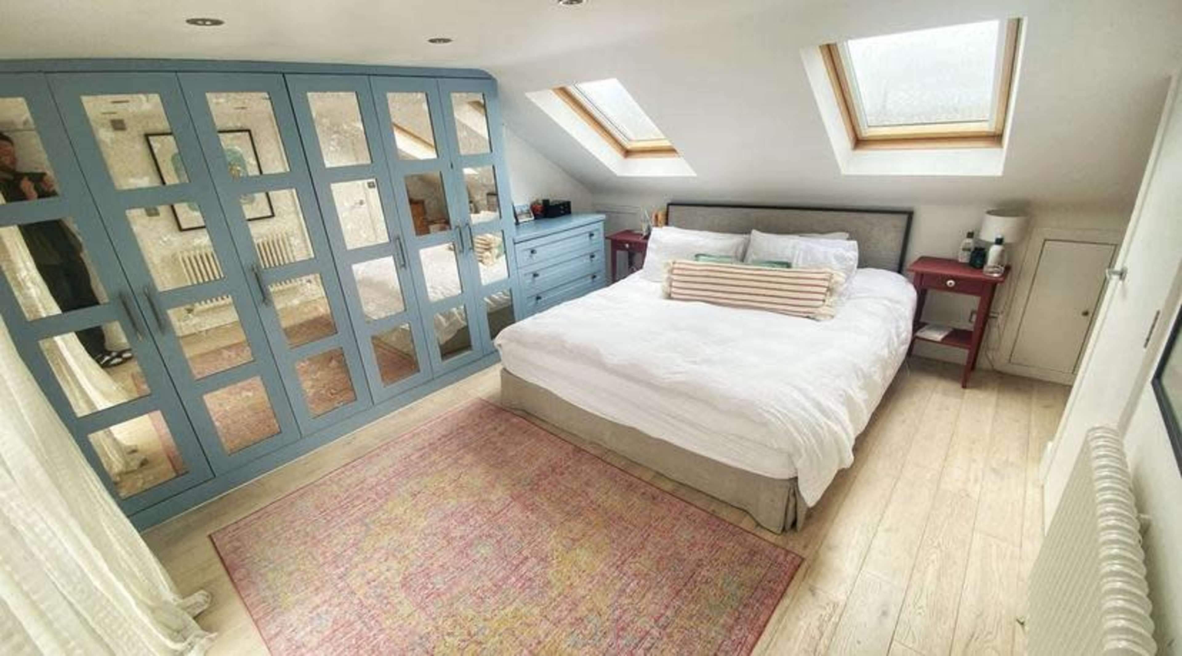 The image shows a cozy bedroom with a large bed, blue-framed closet doors, and skylights.