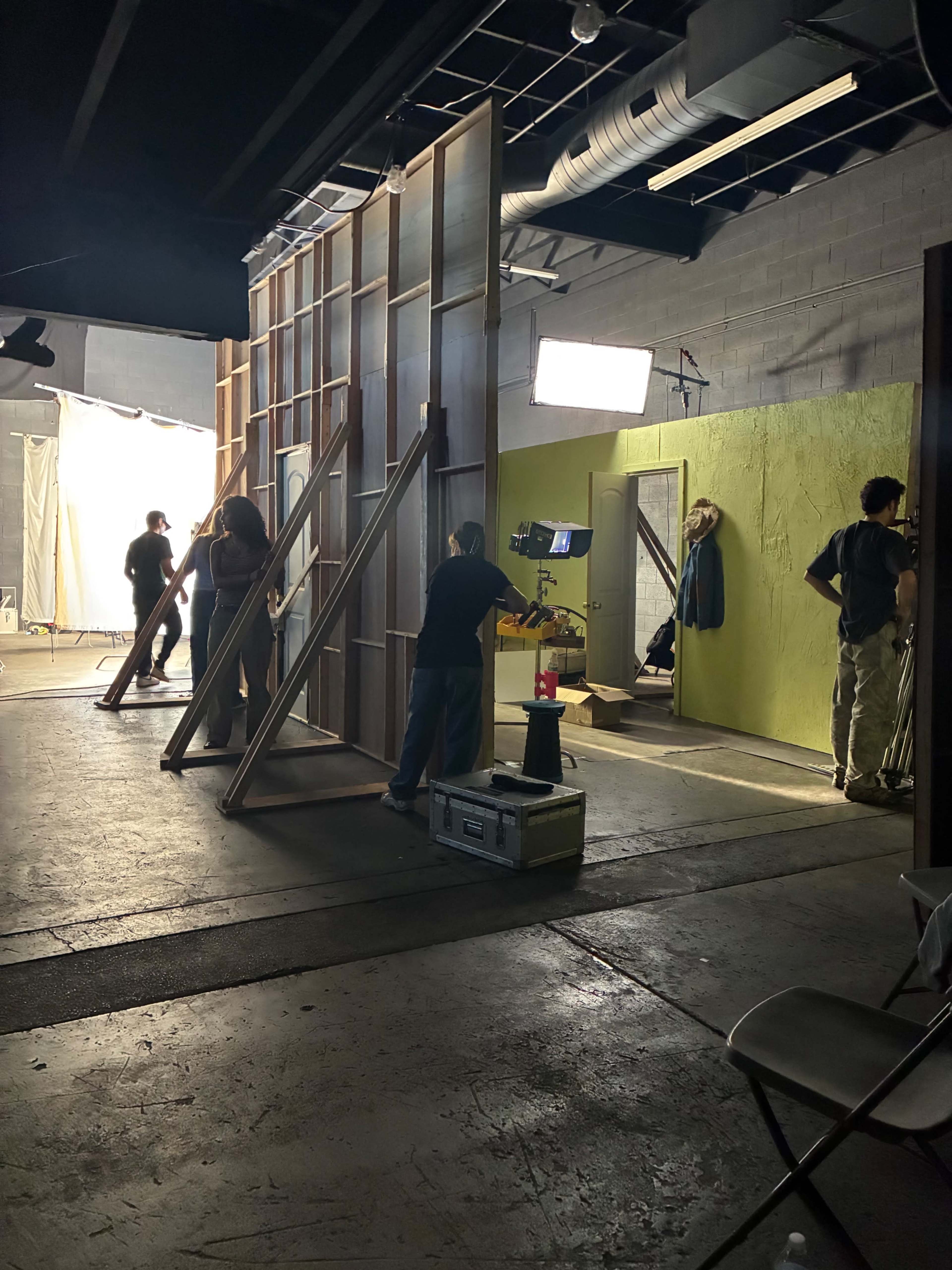 A film crew sets up a set with wooden frames and lighting equipment in a studio space.