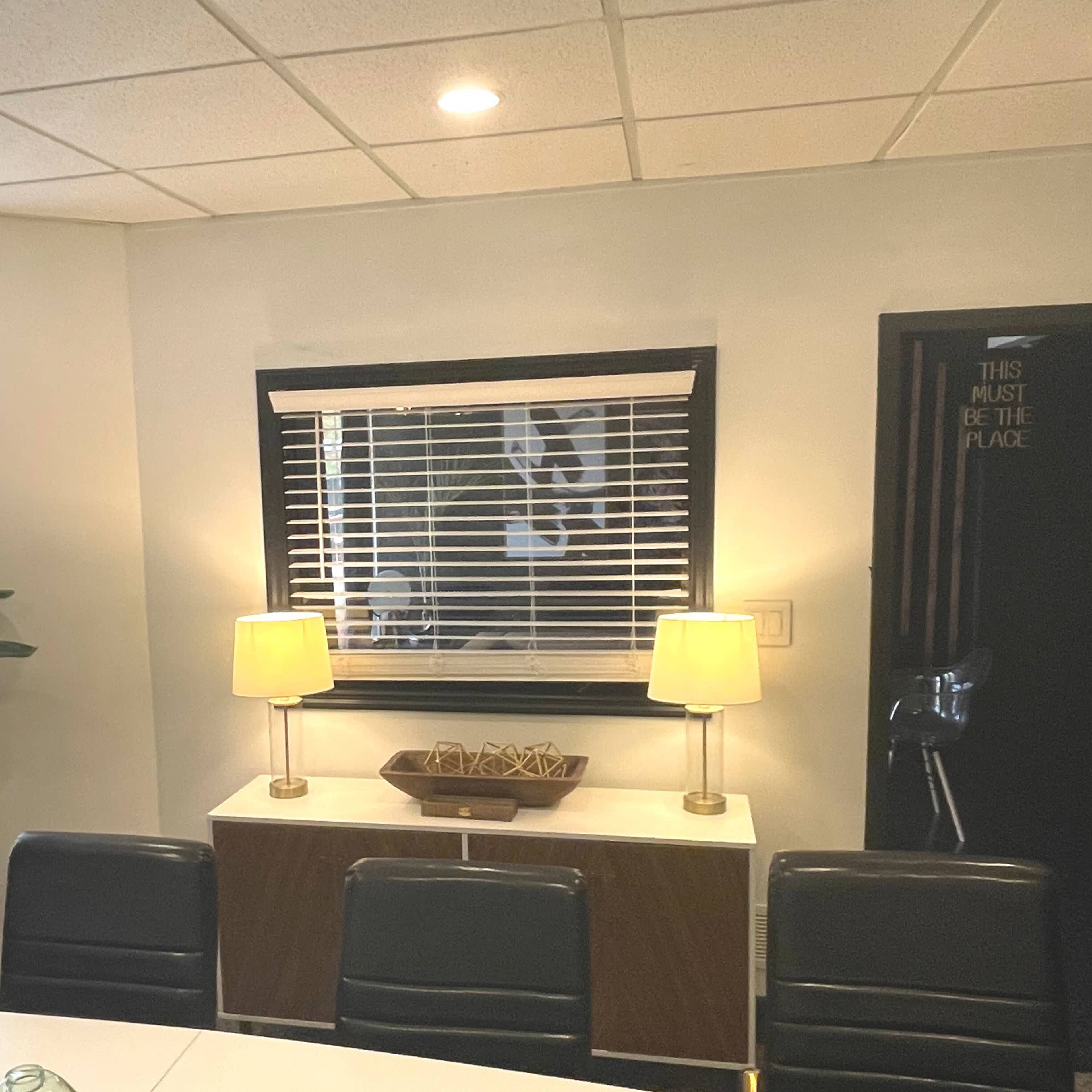 The image shows a modern office space featuring a console table with lamps, a decorative bowl, and a window with blinds.