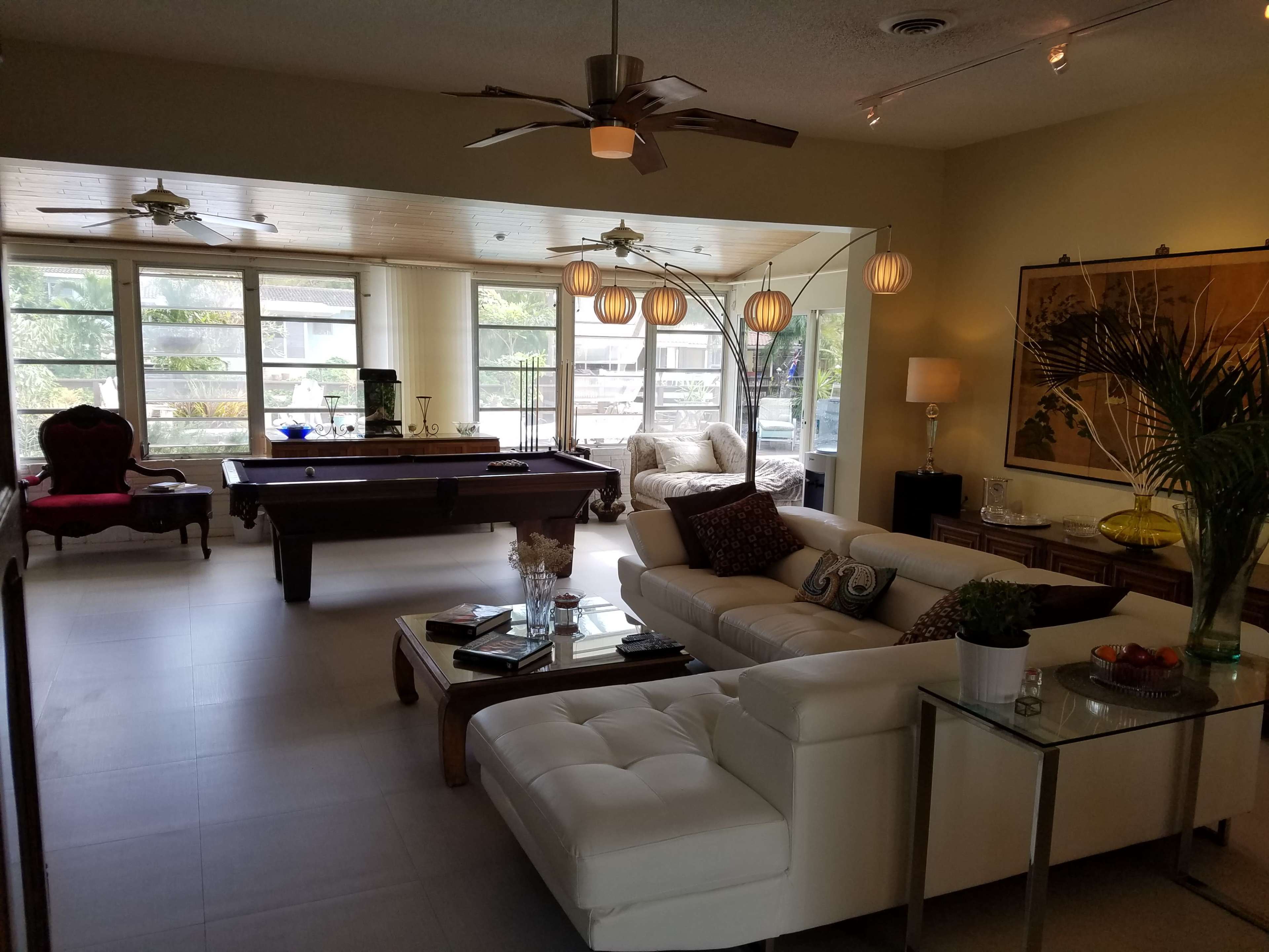 The room features a modern living space with a pool table, large windows, and a mix of seating arrangements including a white sectional sofa and an armchair.