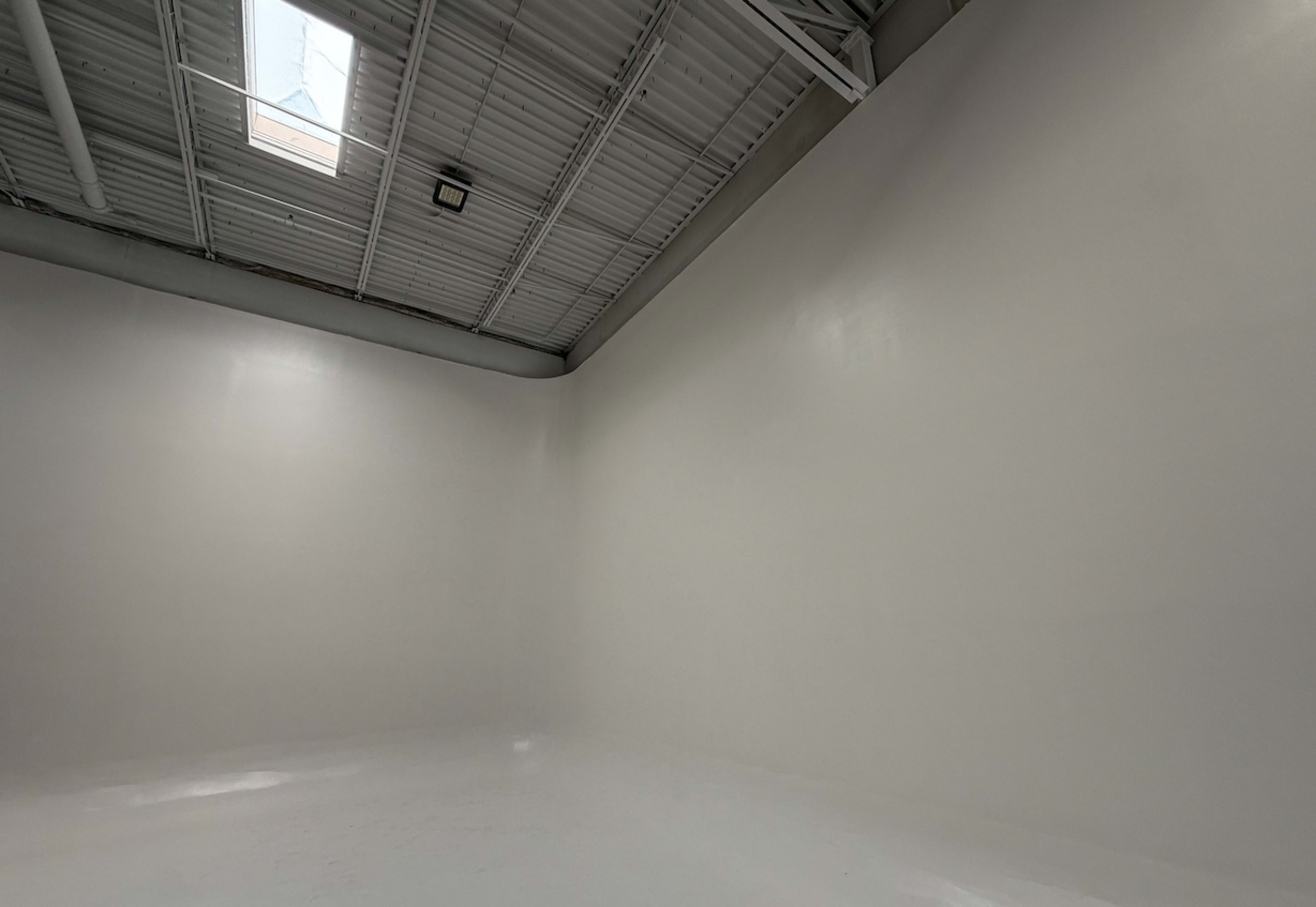 The image shows a spacious, empty room with white walls and a skylight.
