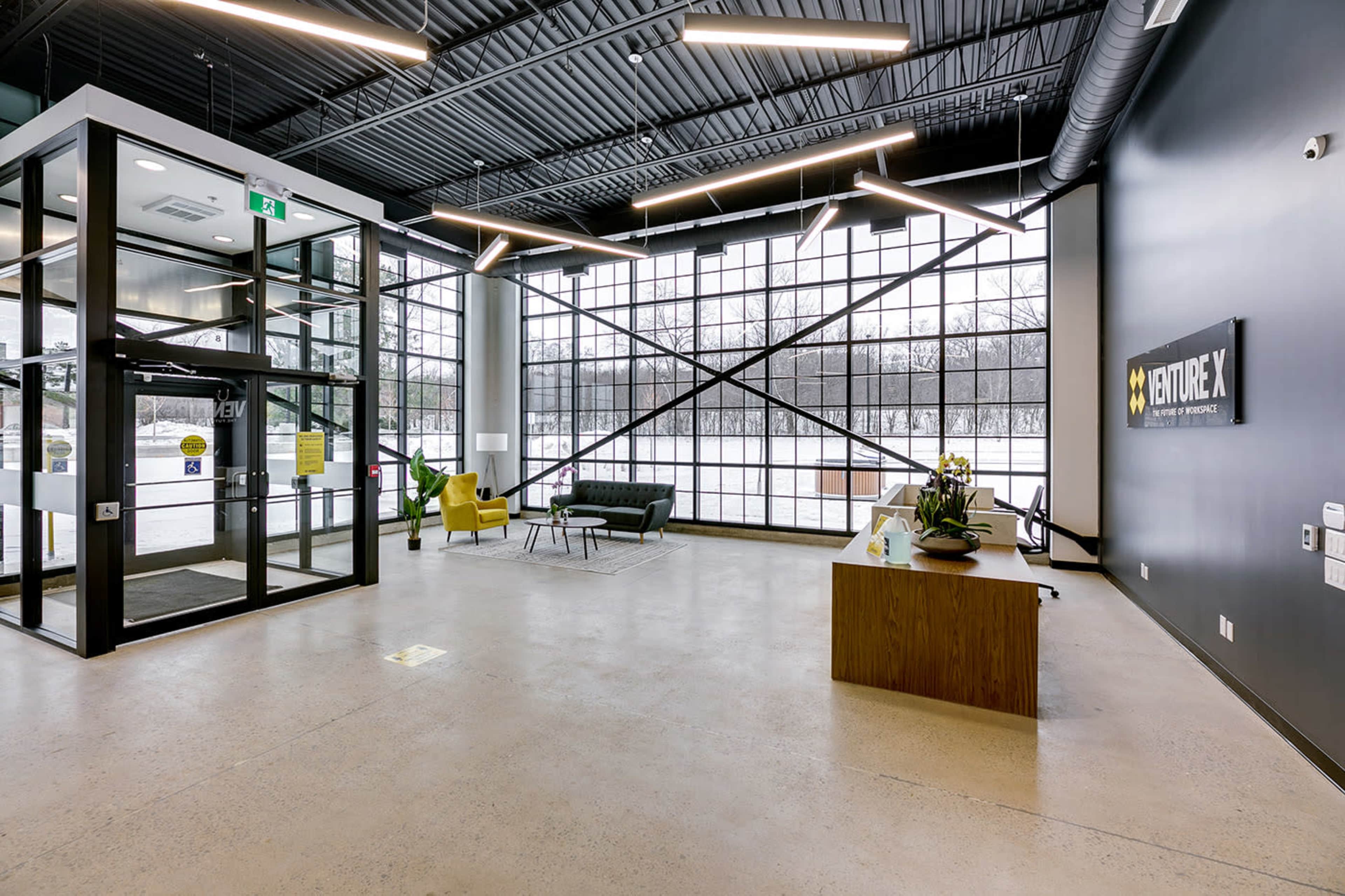 A modern lobby with large windows, industrial-style lighting, a reception area with a plant, and seating arrangements.