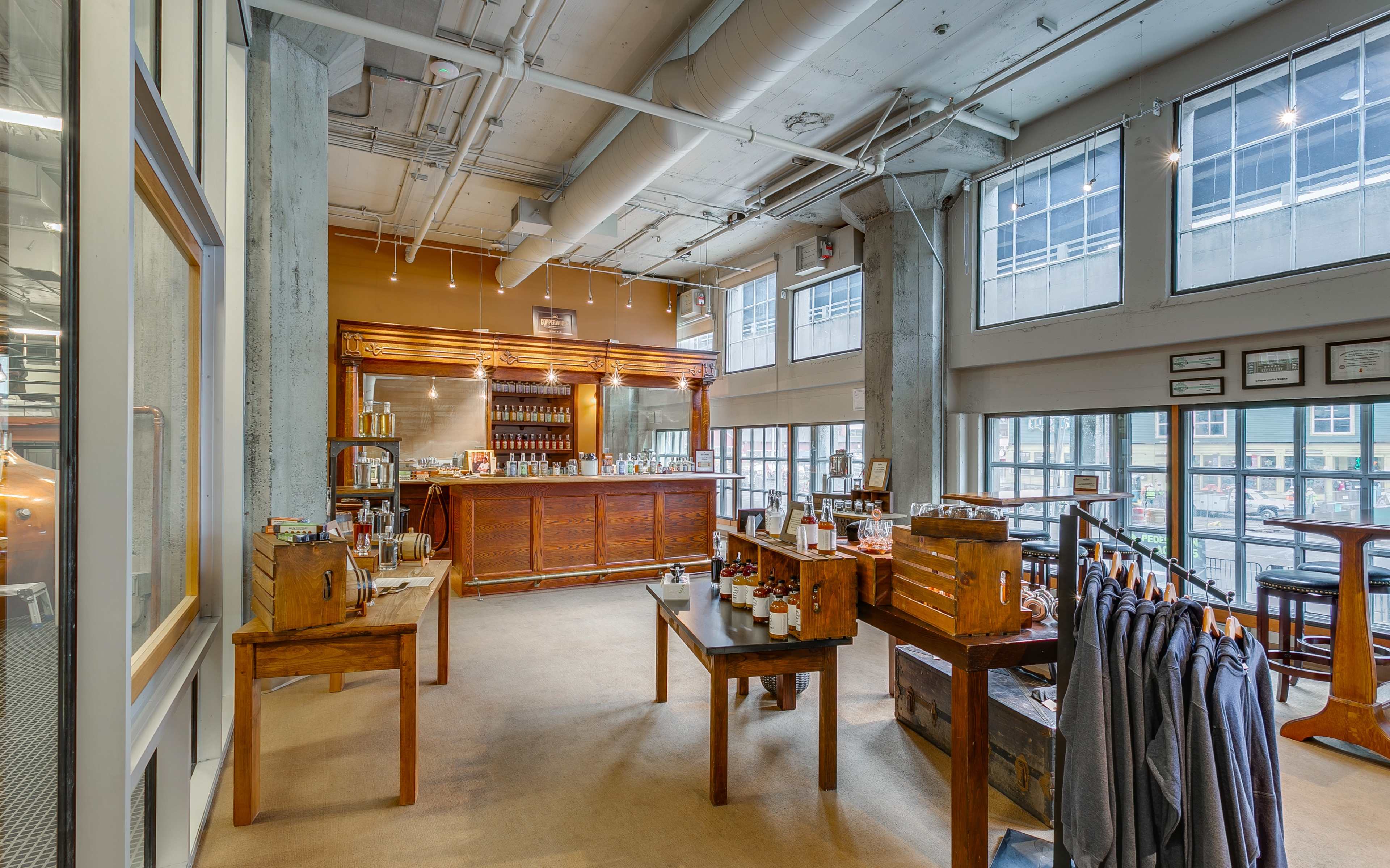 A spacious interior of a cafe features wooden furniture, a sleek bar, and large windows that allow natural light to fill the room.