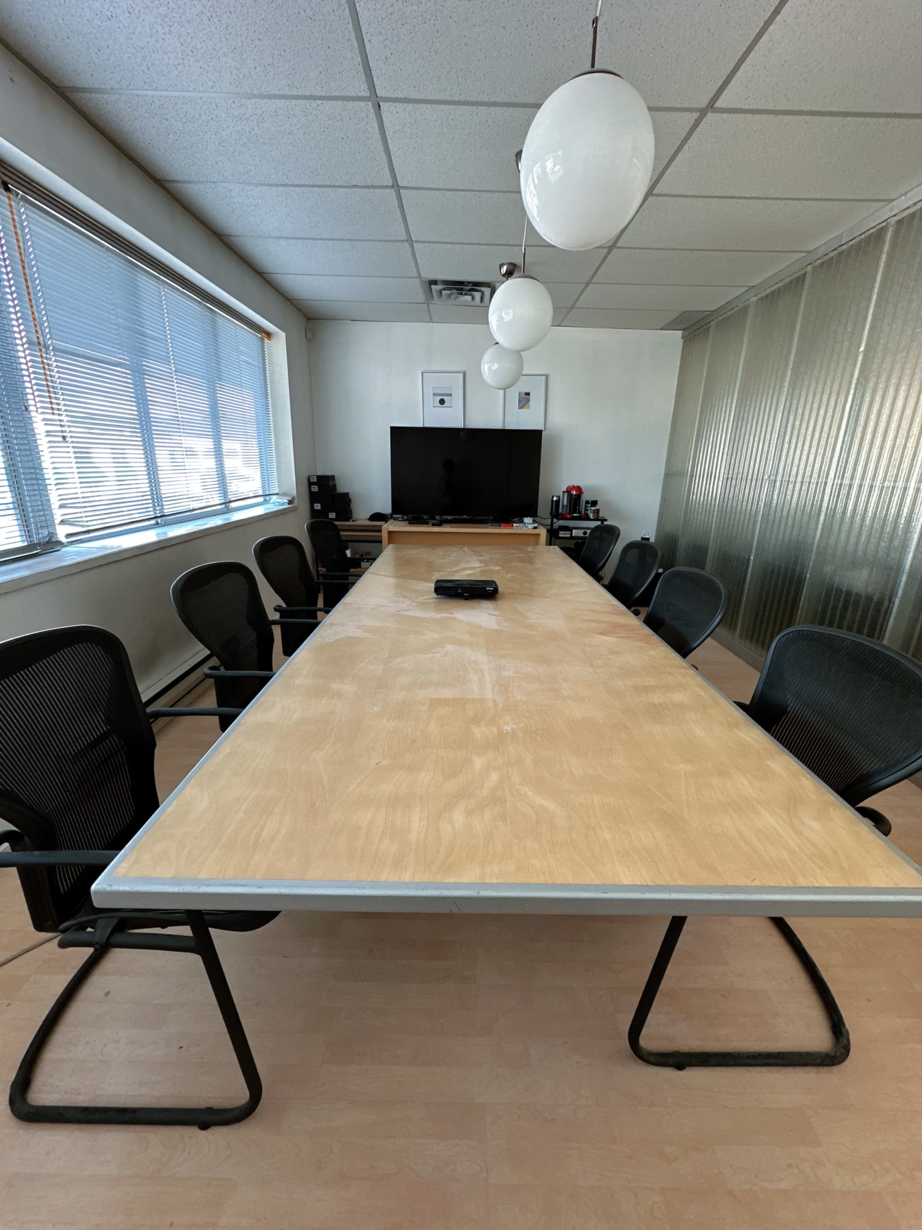 The image shows a long conference table surrounded by black office chairs in a well-lit meeting room.