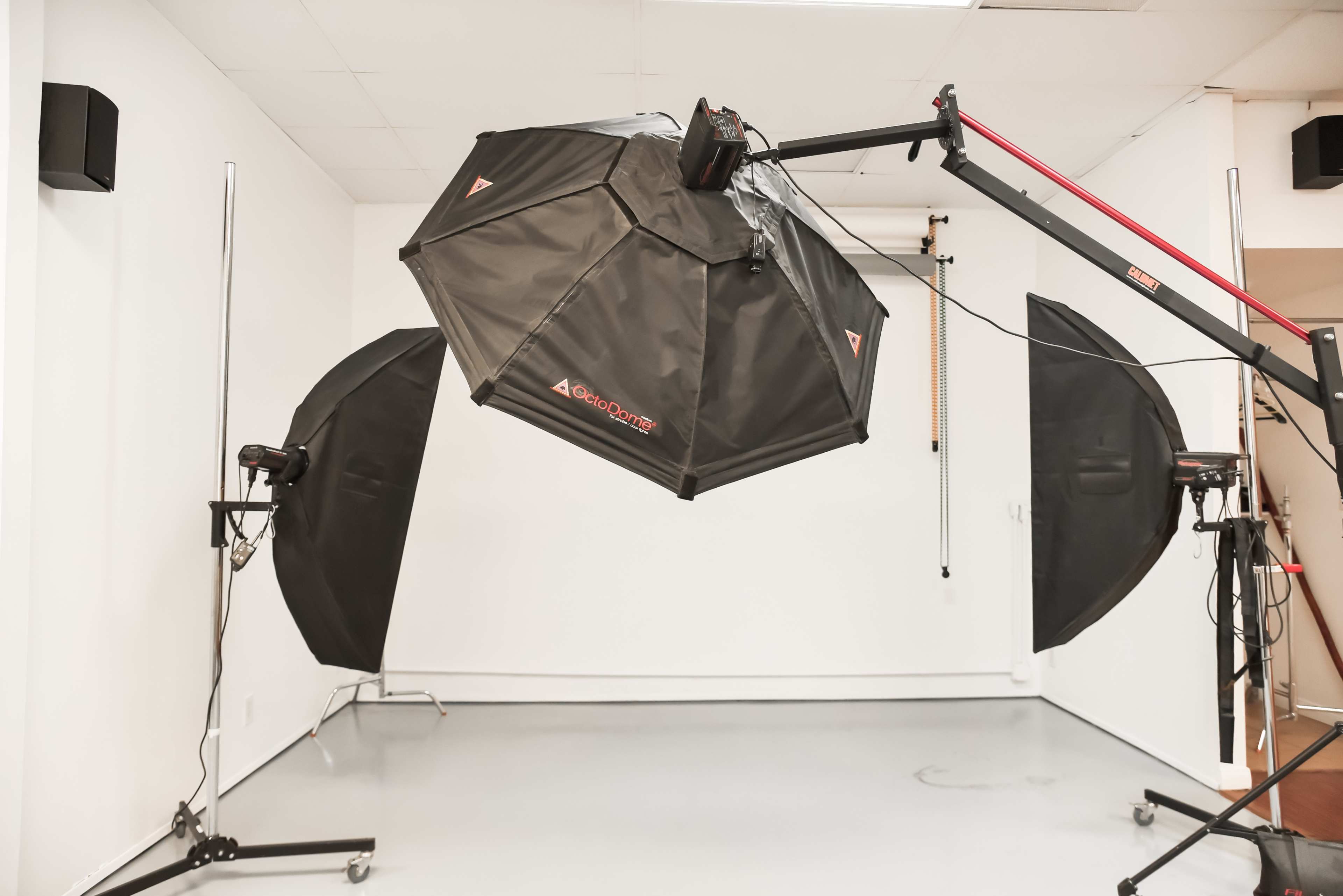 A large octagonal softbox with light stands is set up in a spacious photography studio with a blank wall.