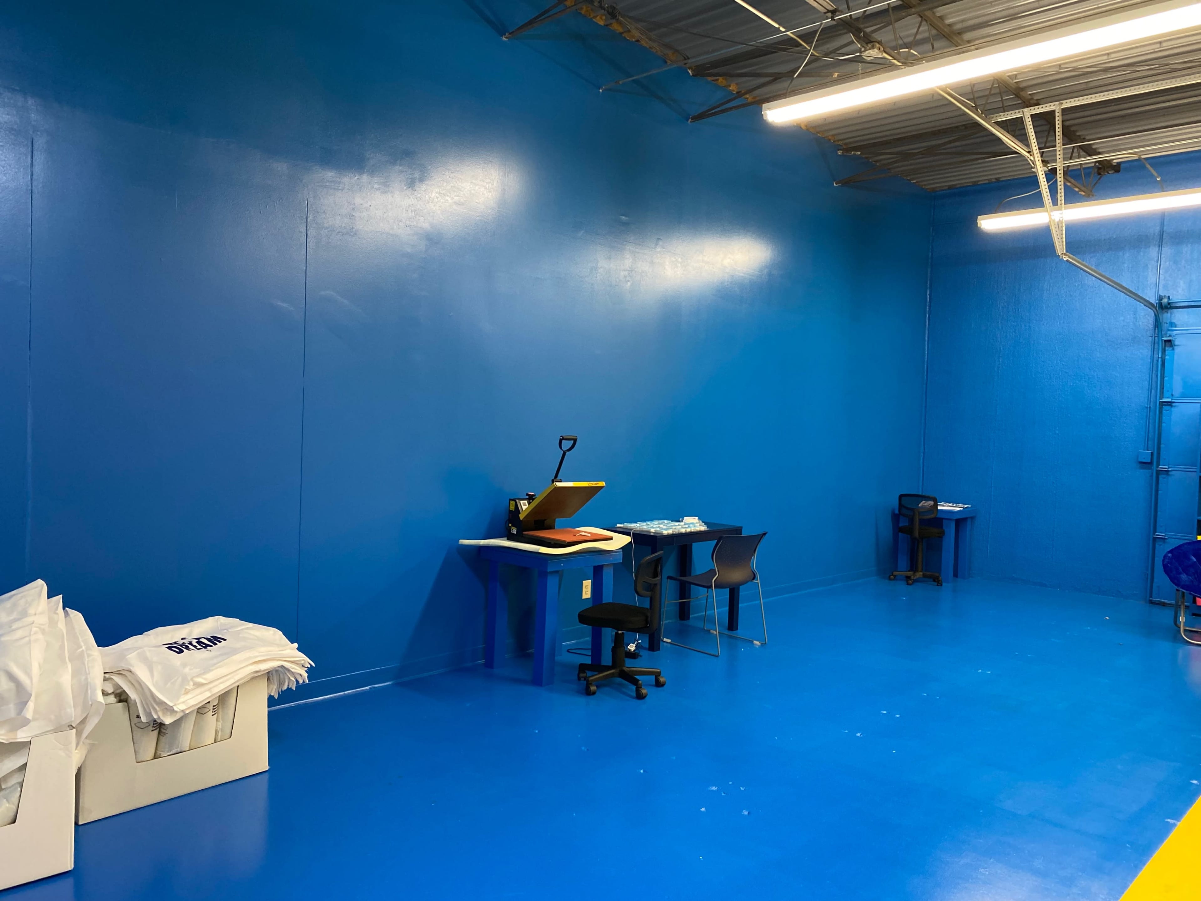 A blue-painted room with two tables, a chair, and stacks of white items in the corner.
