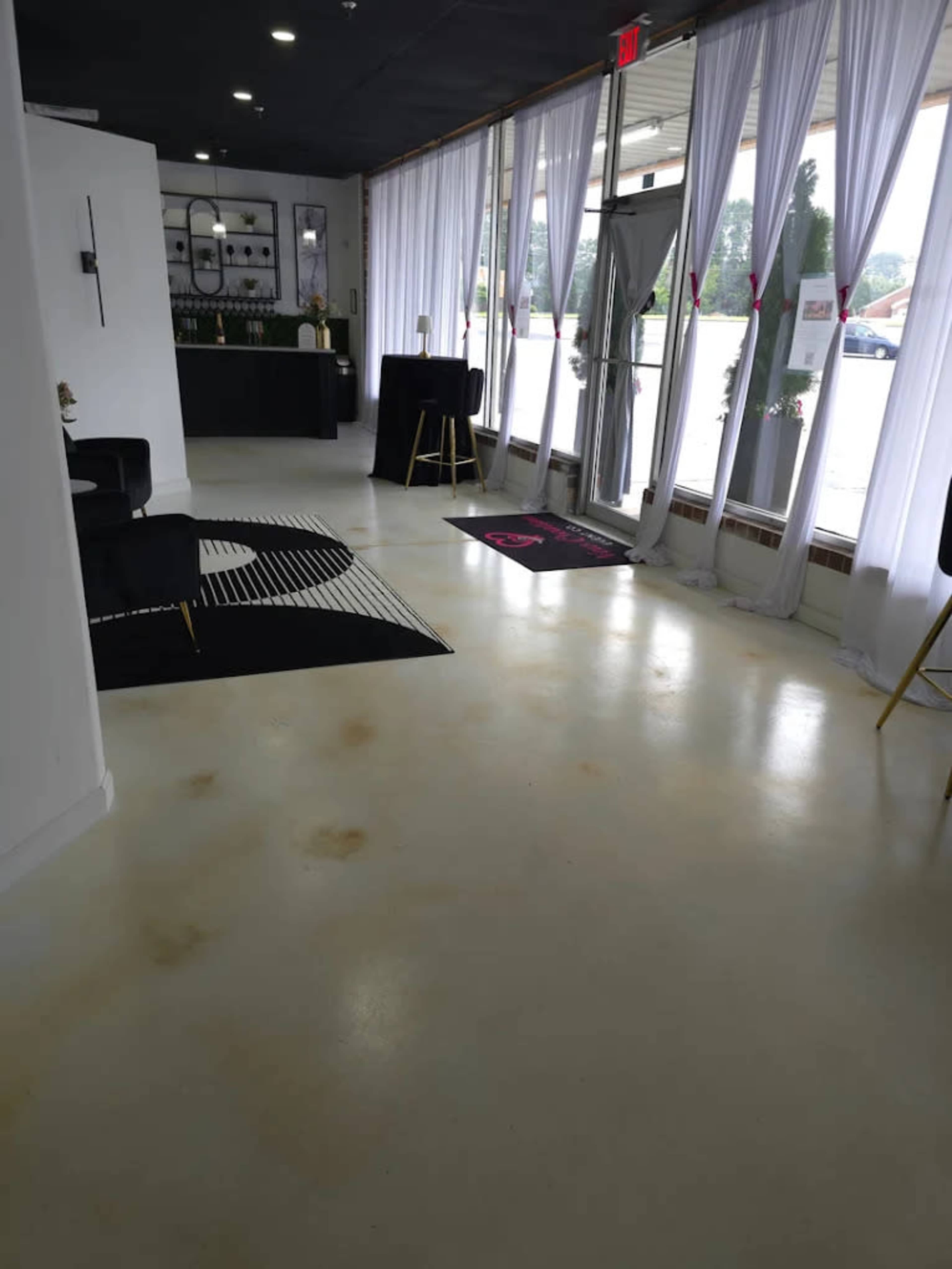 The image shows a spacious interior with a polished floor, white curtains, and a reception area in the background featuring black furniture and decor.