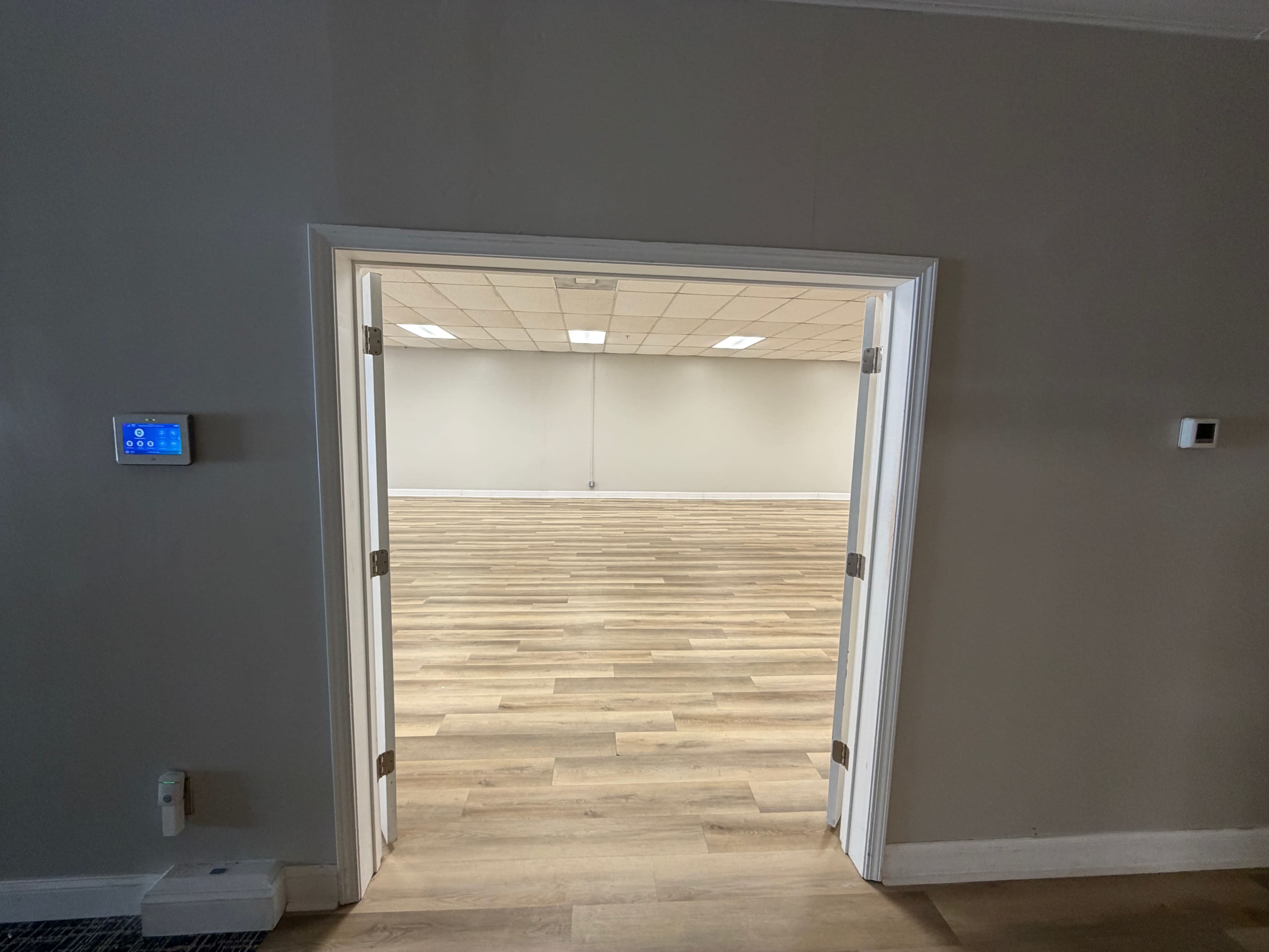 The image shows an open doorway leading into a spacious room with wooden flooring and plain walls.