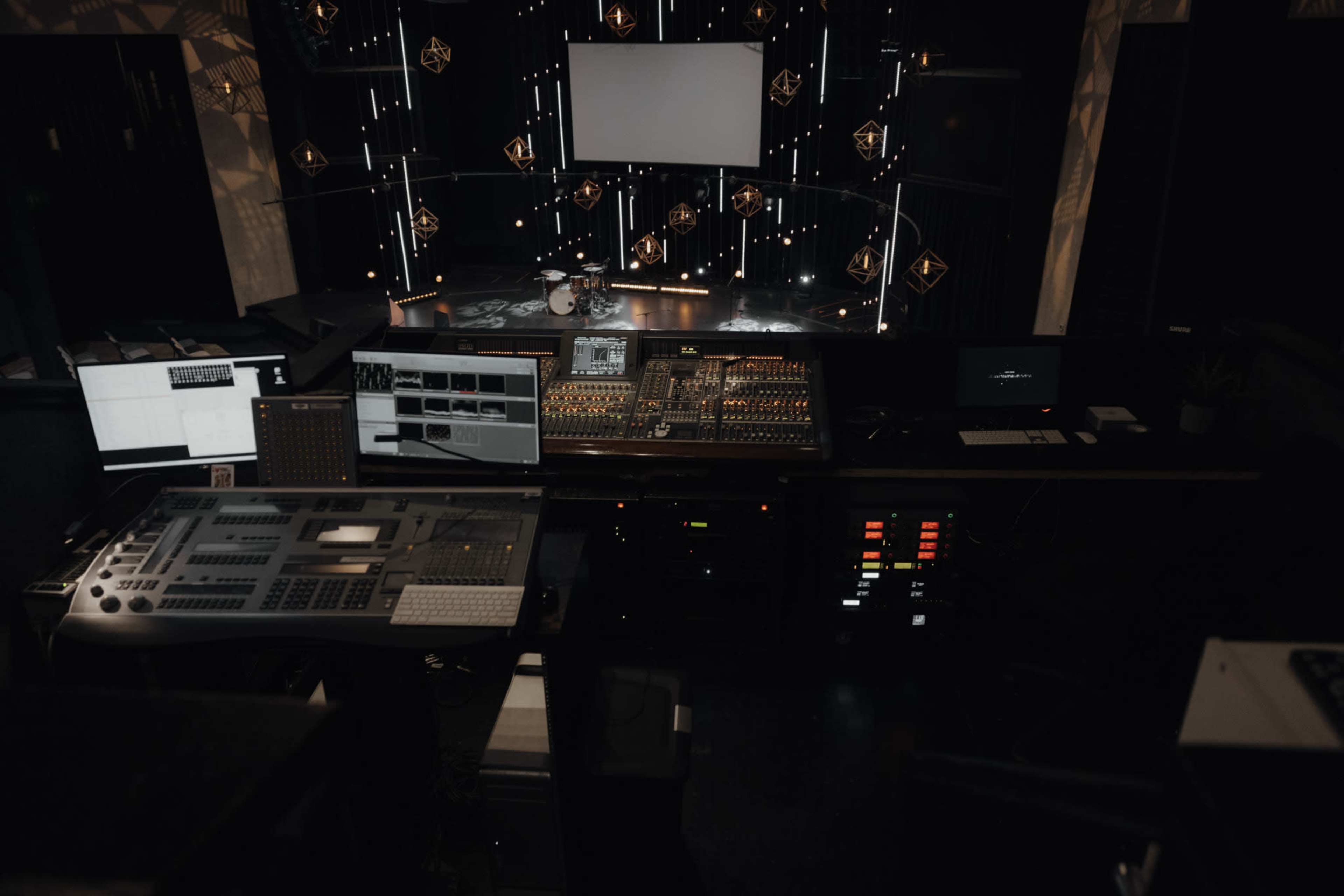 A sound and lighting control room with various screens and equipment in front of a performance stage.