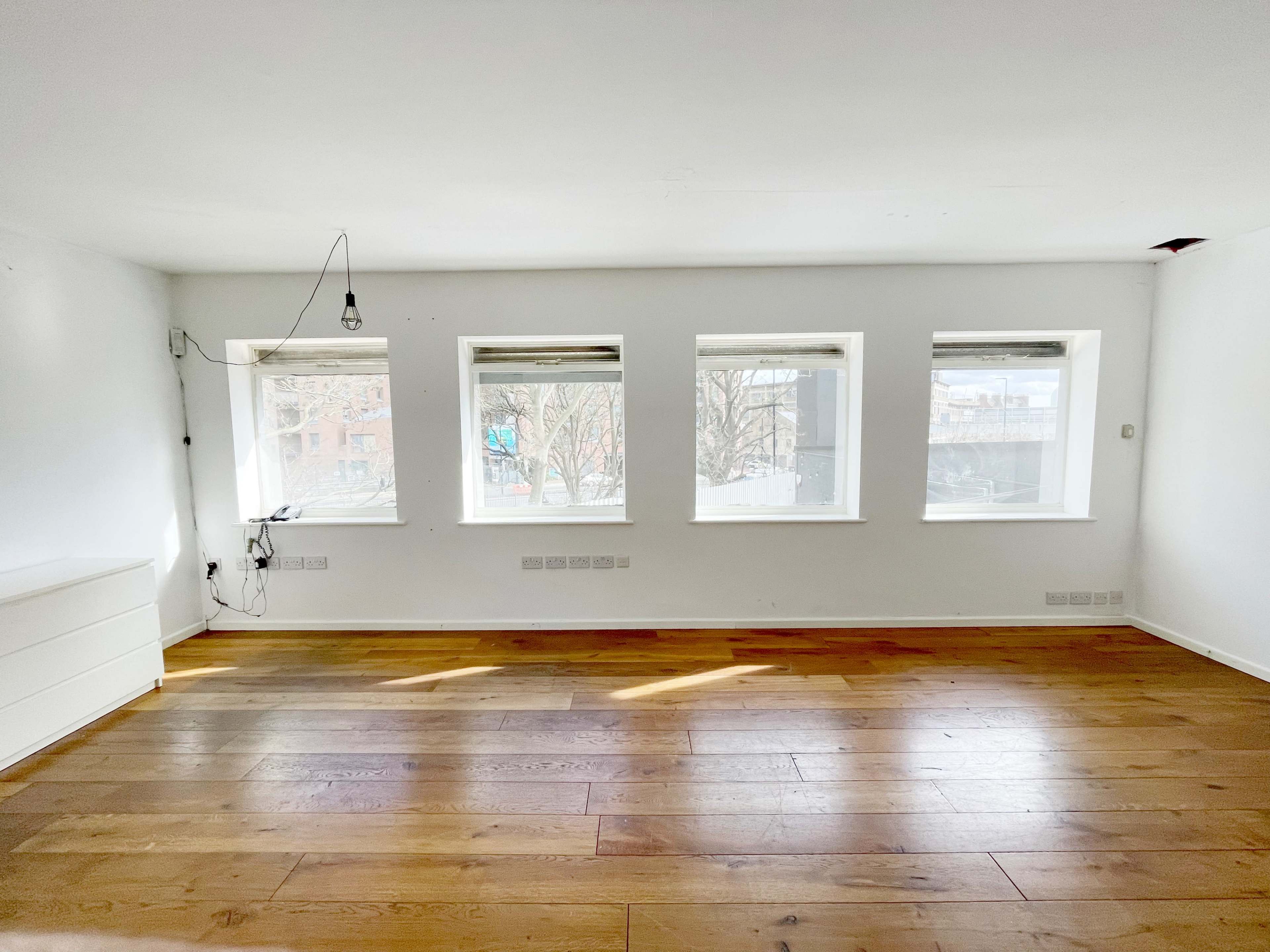 An empty room with hardwood floors and four windows providing natural light.