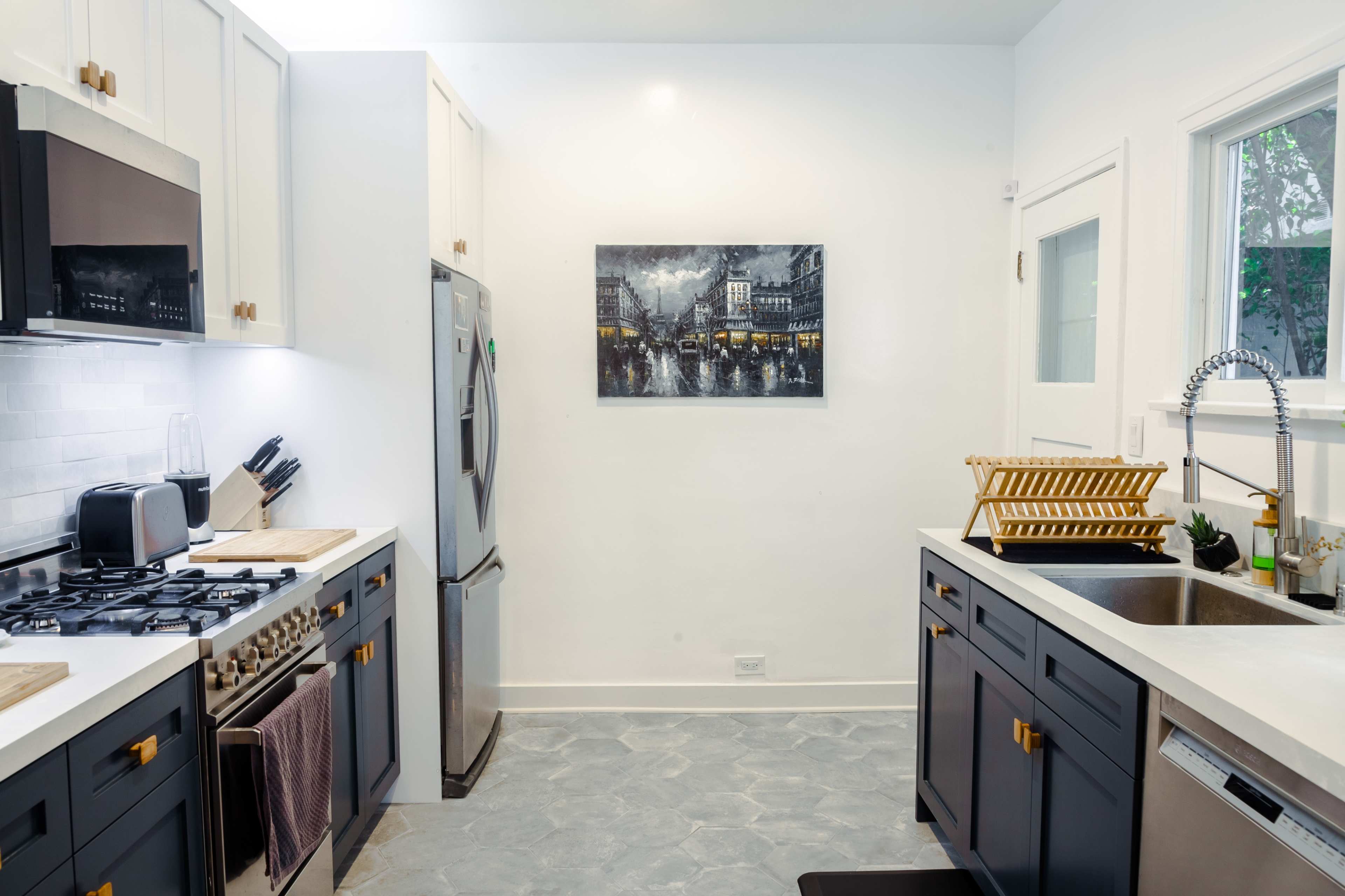 A modern kitchen features stainless steel appliances, dark cabinetry, and a wall-mounted black-and-white cityscape photograph.