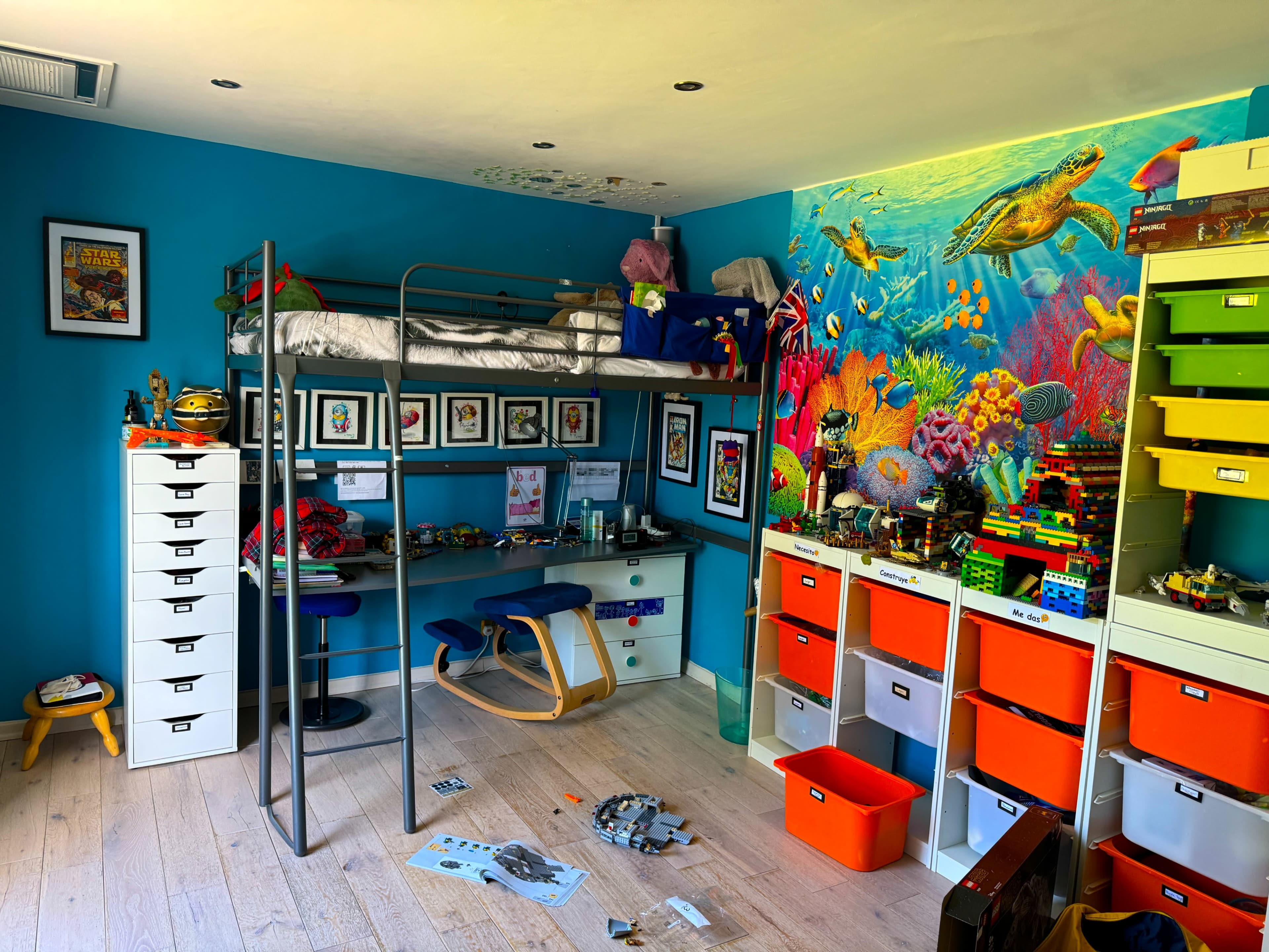 The image shows a colorful children's bedroom featuring a loft bed, a desk with a chair, and vibrant storage units filled with toys and decorations.