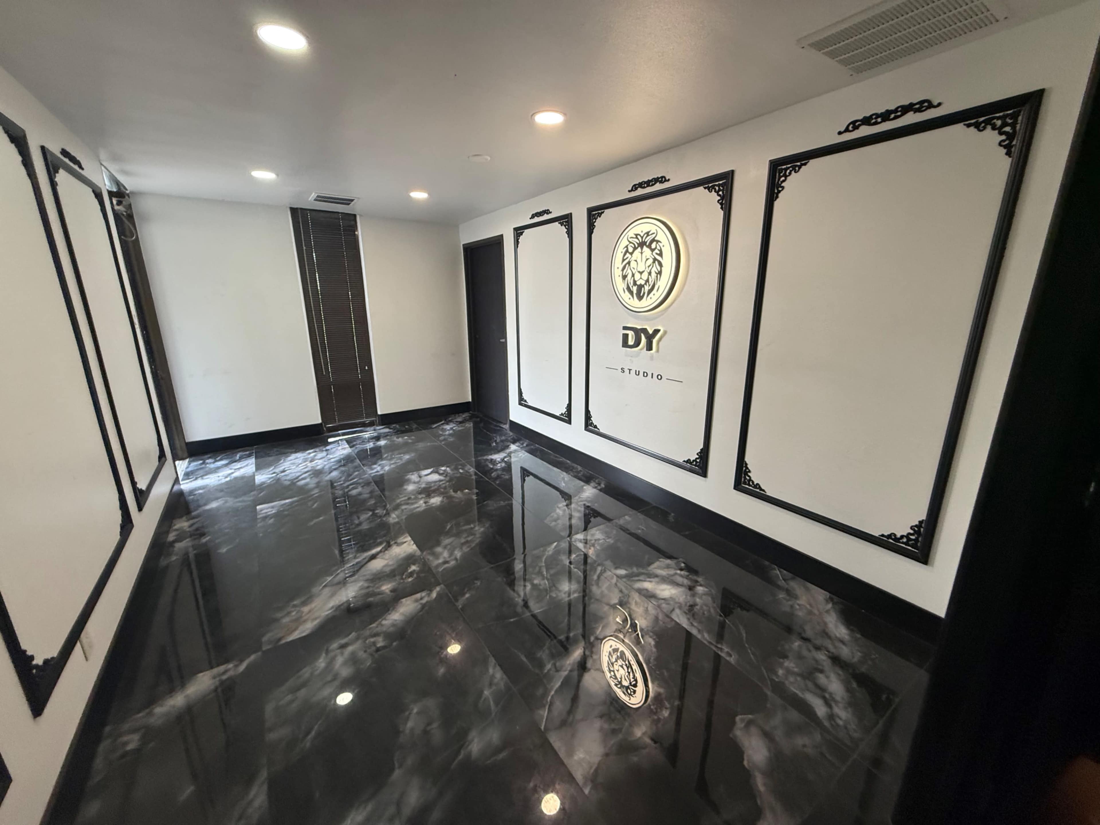 The image shows a modern, empty room with black marble flooring and white walls featuring decorative borders and a logo on one wall.