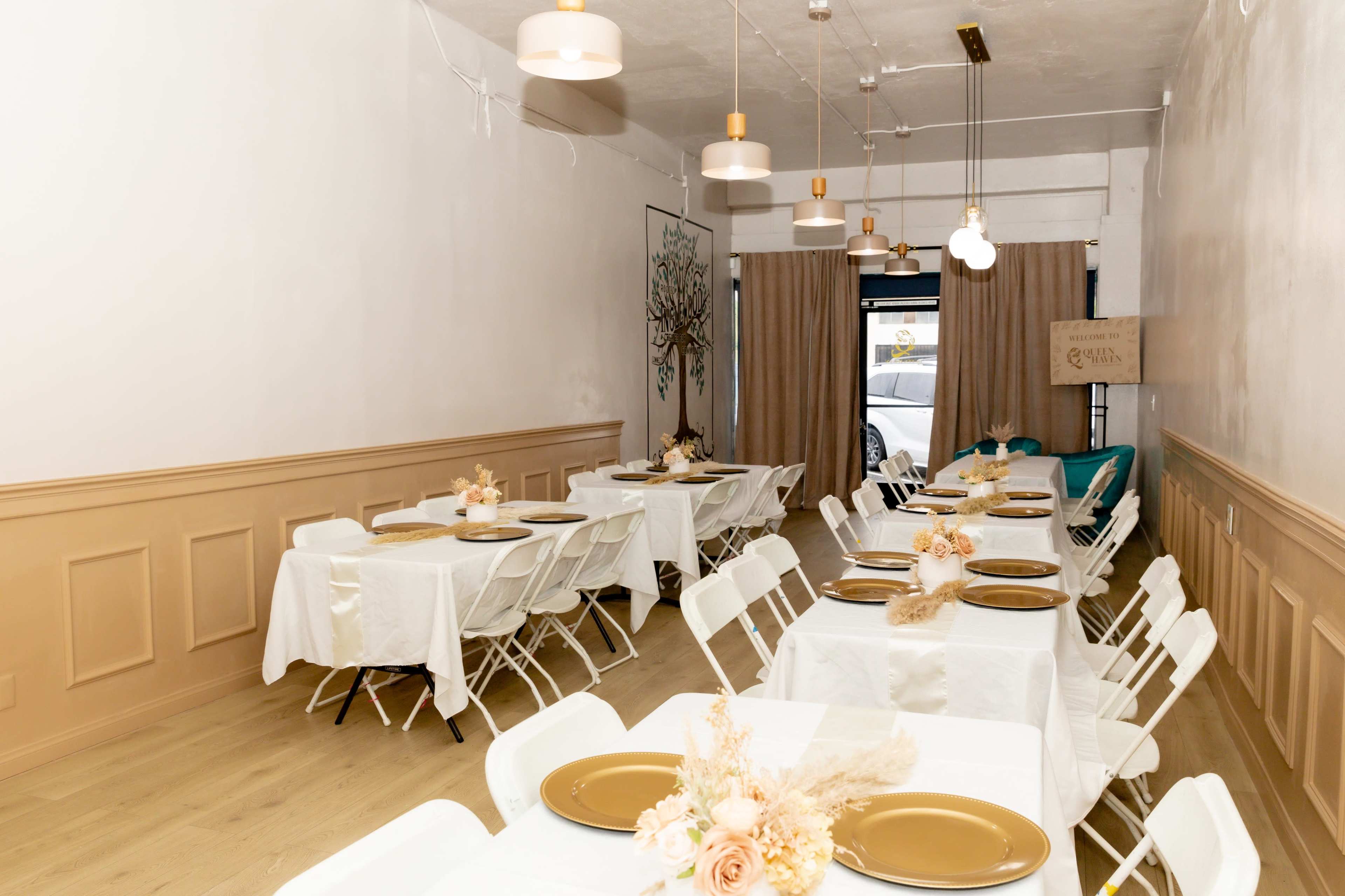 The image shows a neatly arranged dining area with white tables and chairs, decorated with centerpieces and elegant lighting.