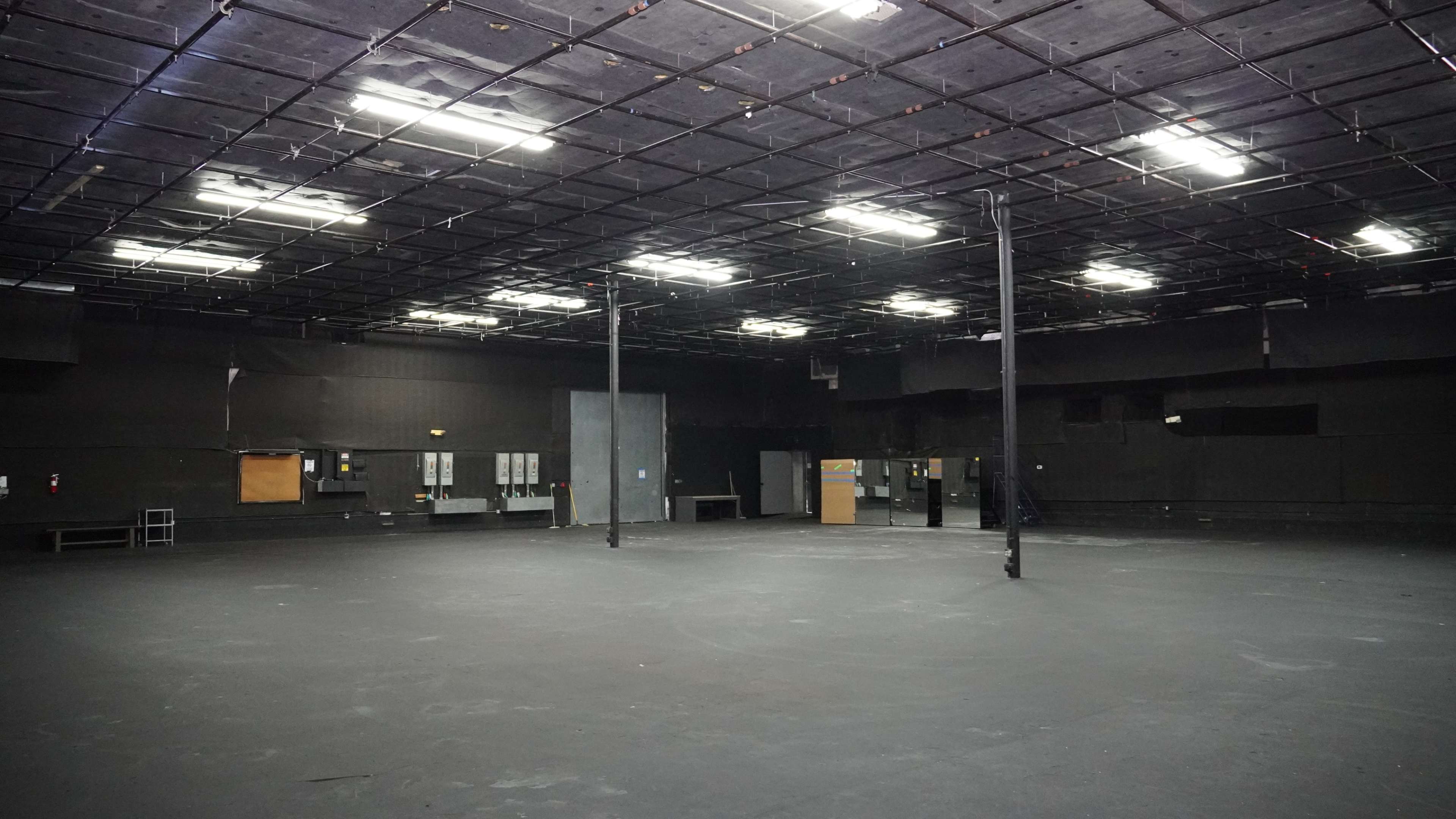 The image shows a large, empty black room with a flat ceiling and fluorescent lights.