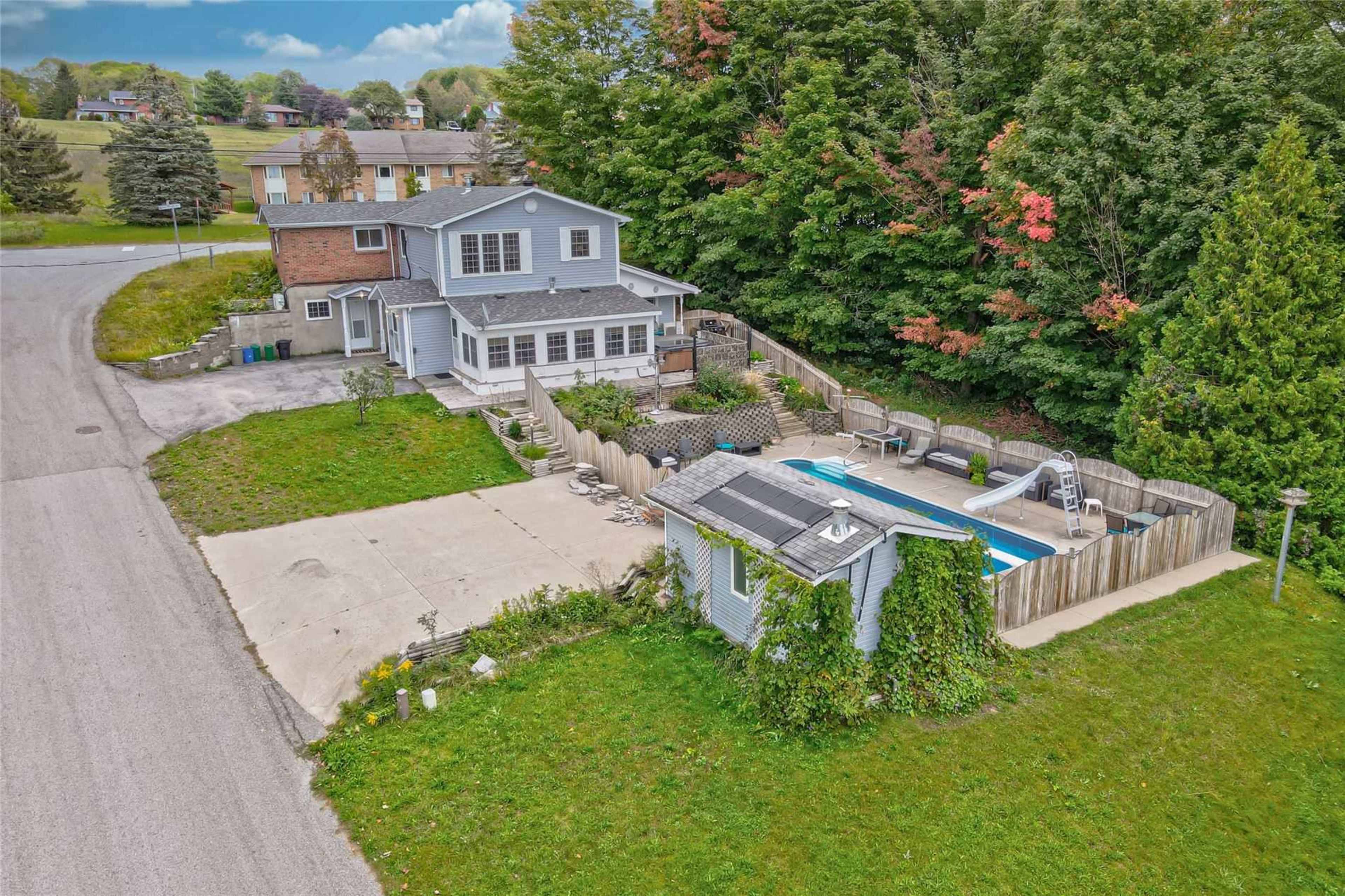 A two-story house with a swimming pool and fenced yard sits at the end of a road surrounded by trees.