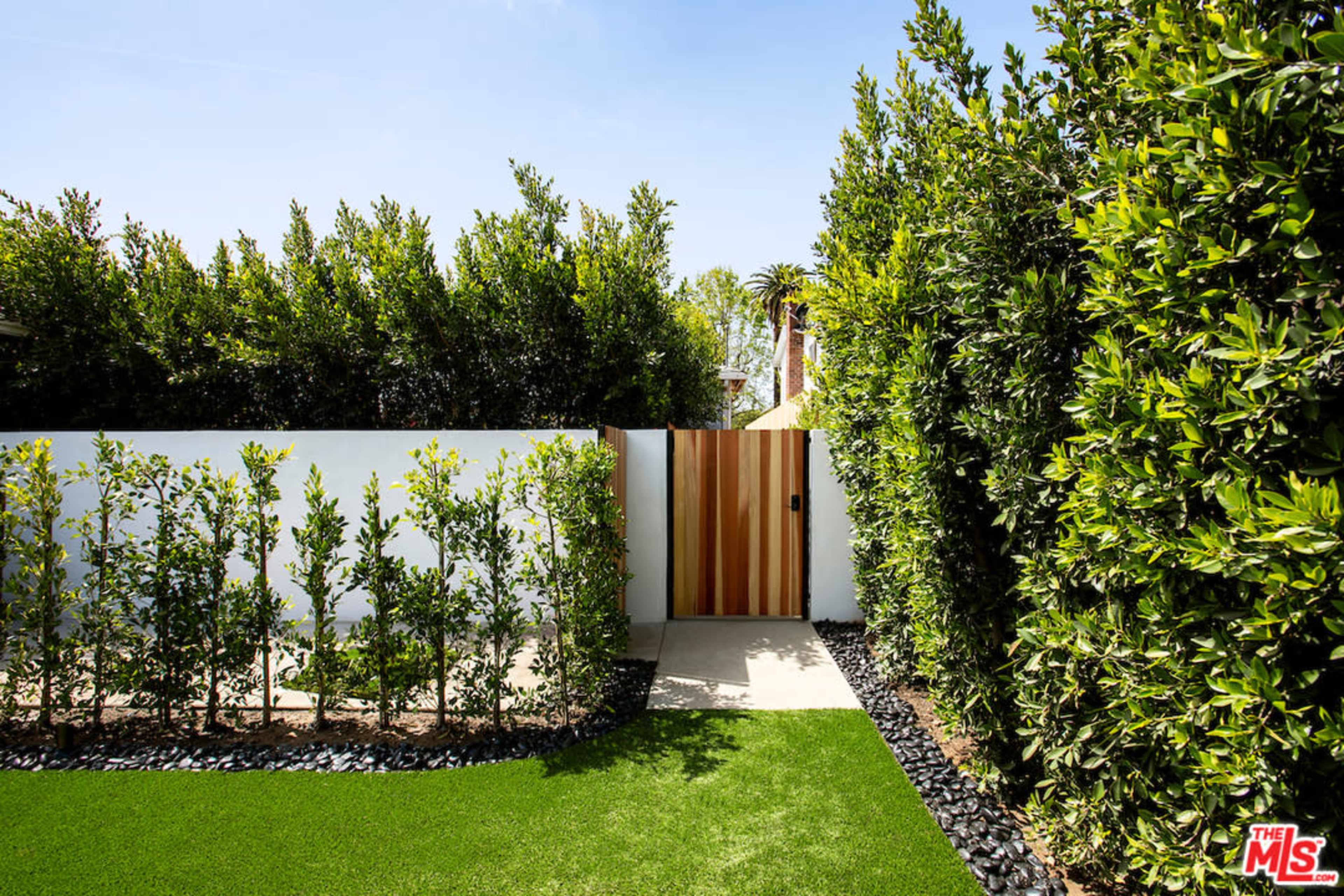 A pathway leading to a wooden gate surrounded by tall hedges and a neatly maintained lawn.
