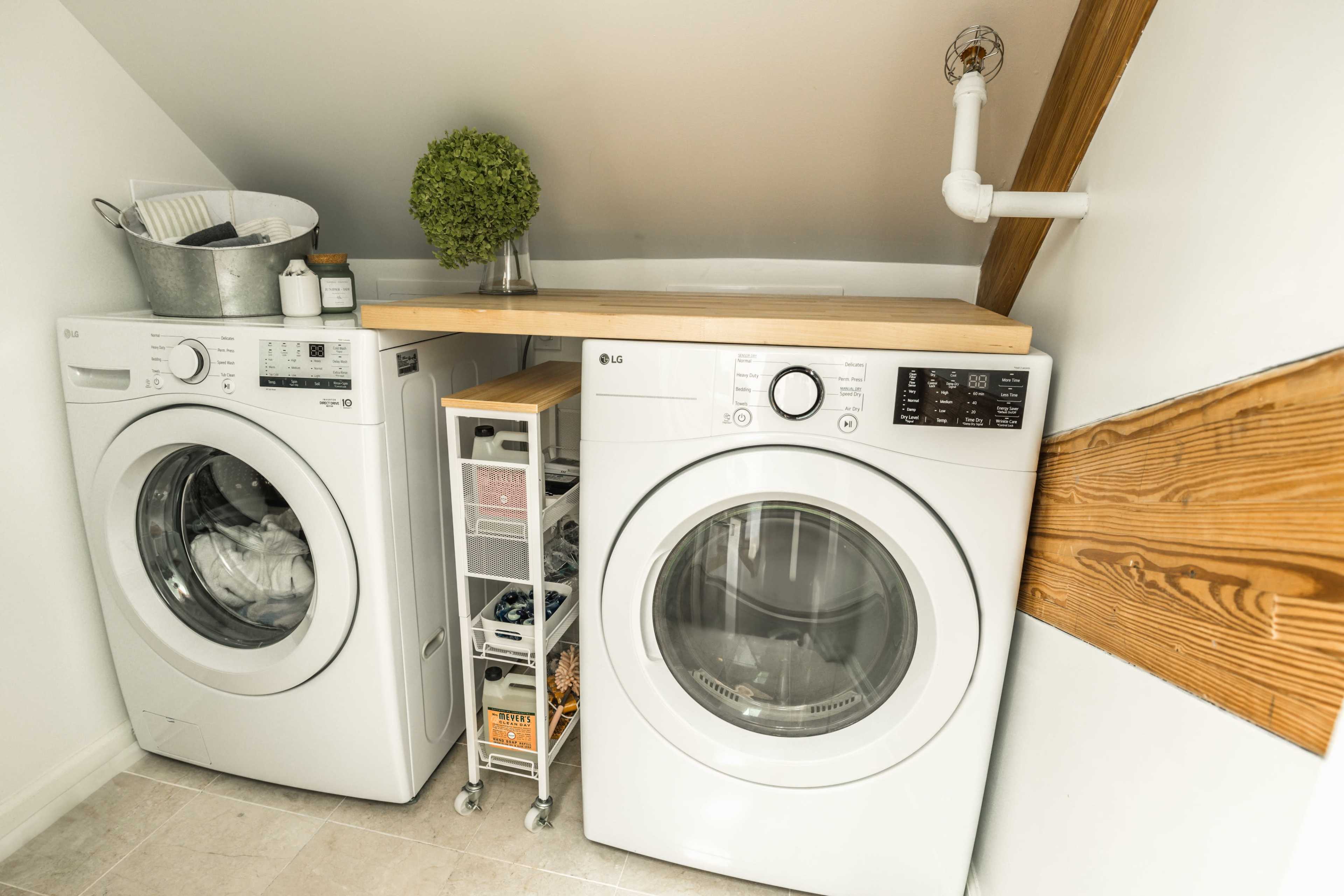 A compact laundry area with a stacked washer and dryer, a wooden countertop, and storage containers underneath.