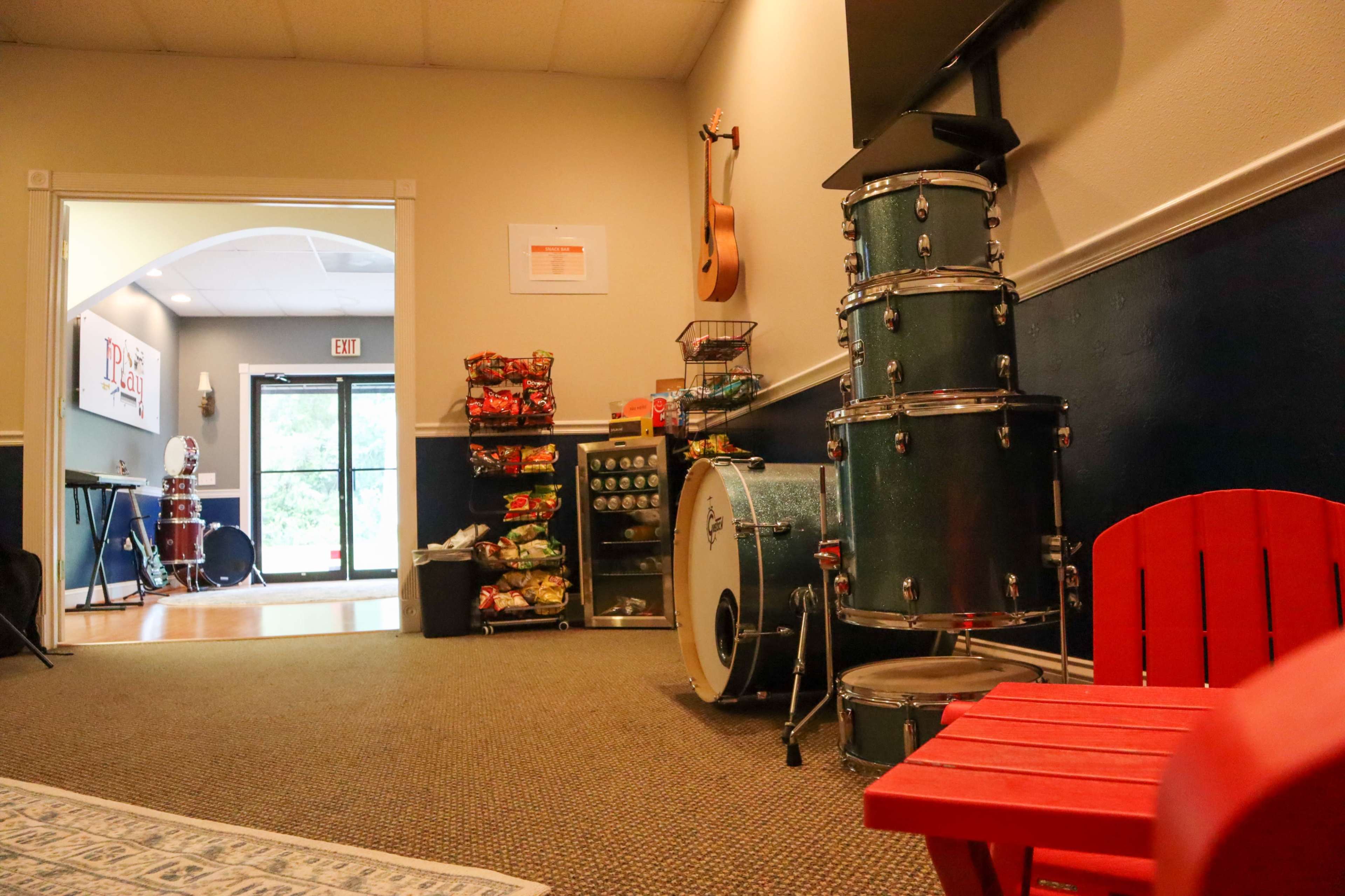 A hallway features a blue and white color scheme, a drum set, and a red children's chair beside a shelf of snacks and beverages.