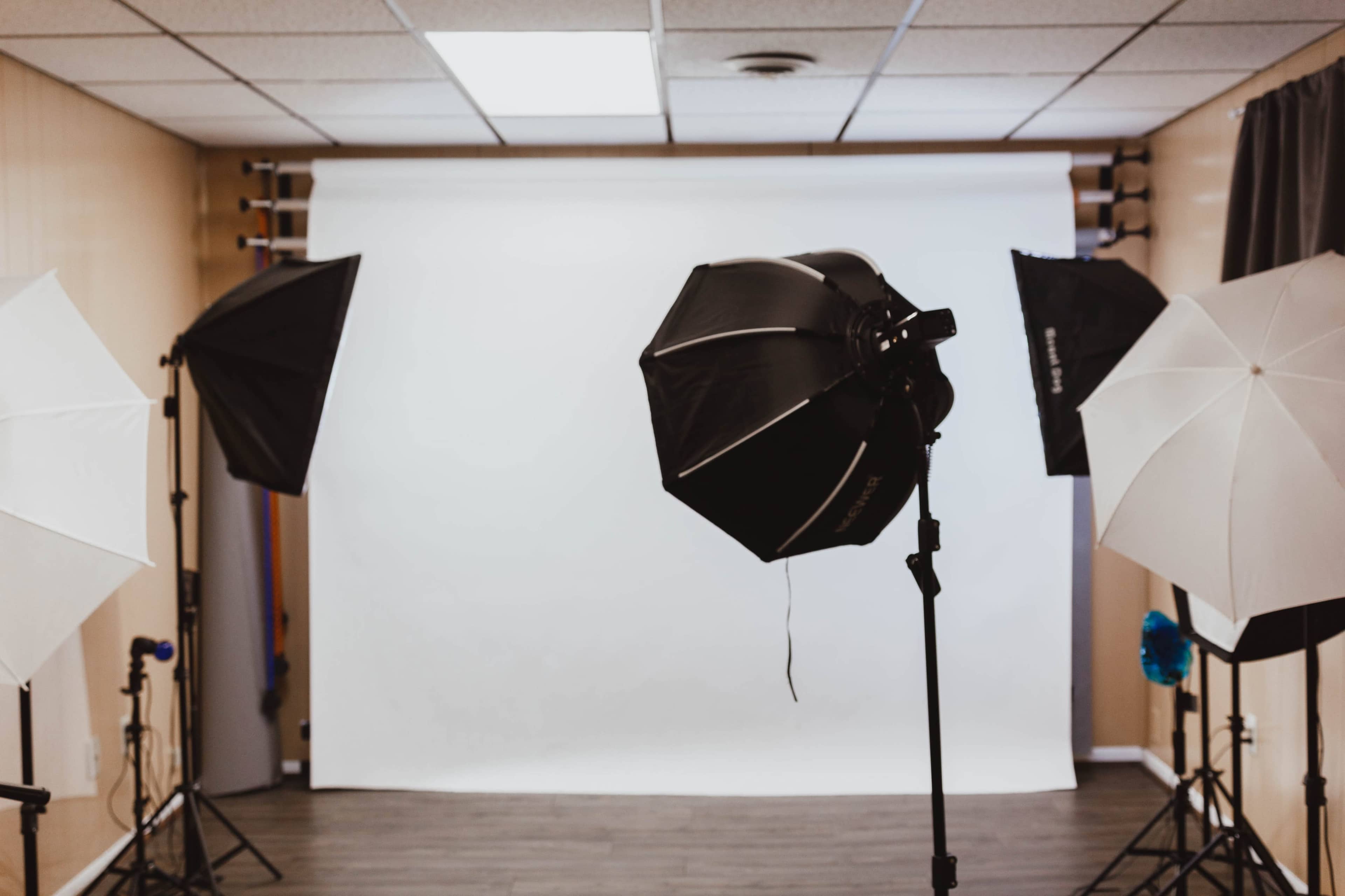 A photography studio is set up with softbox lights and a blank white backdrop.