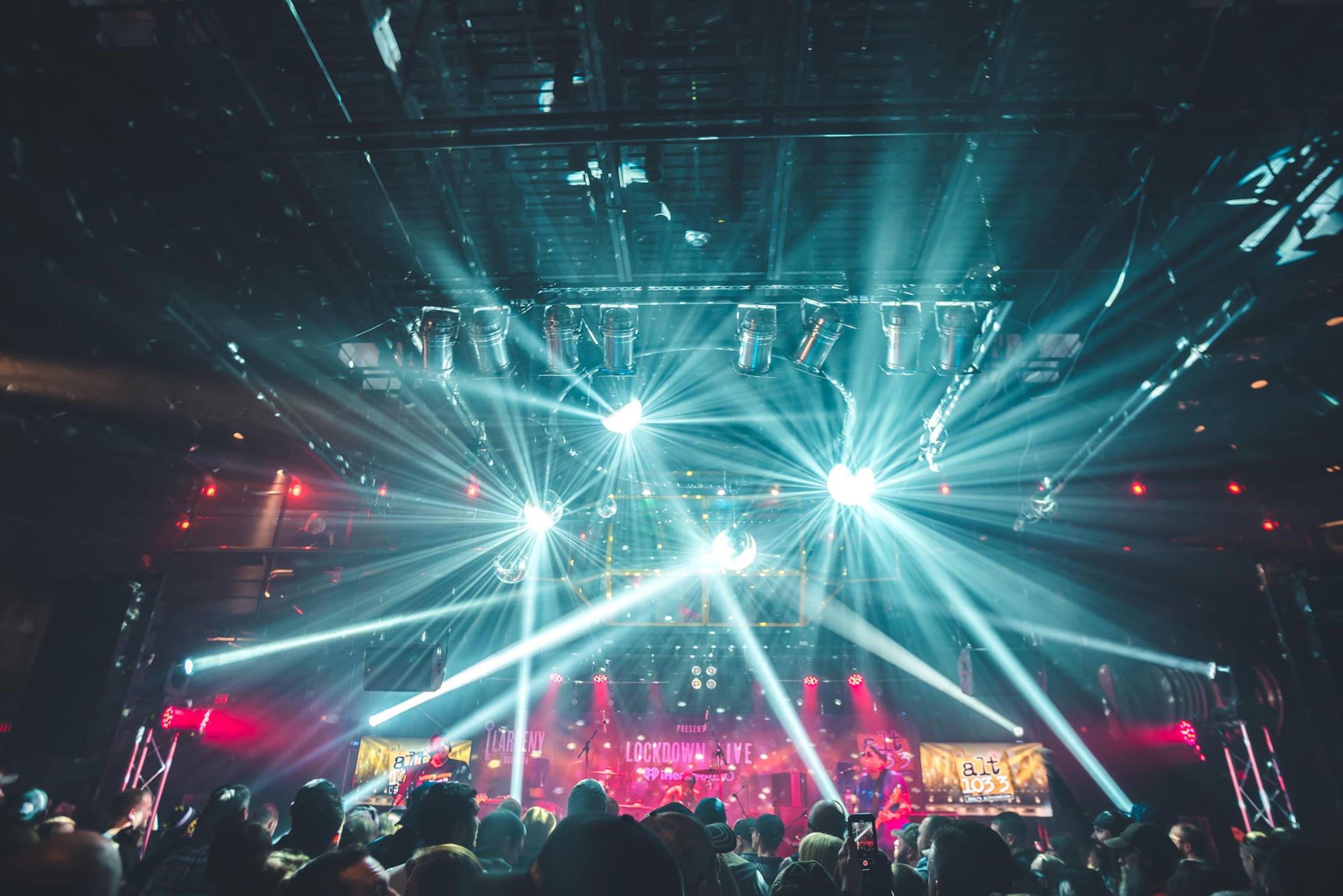A crowd watches a live performance under theatrical lighting in a concert venue.