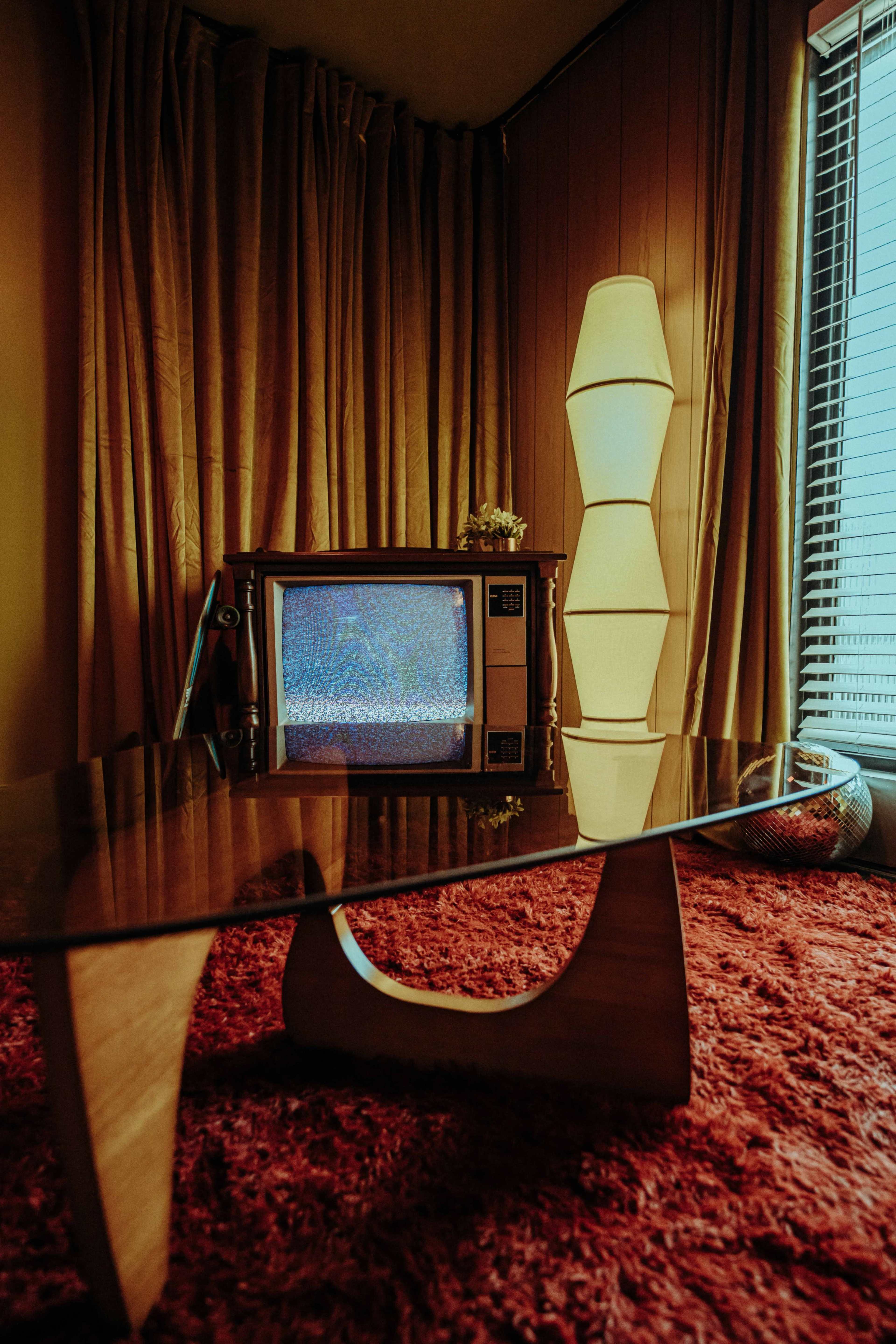 The image features a vintage television set displaying static in a room with golden curtains, a glass coffee table, and a modern lamp.
