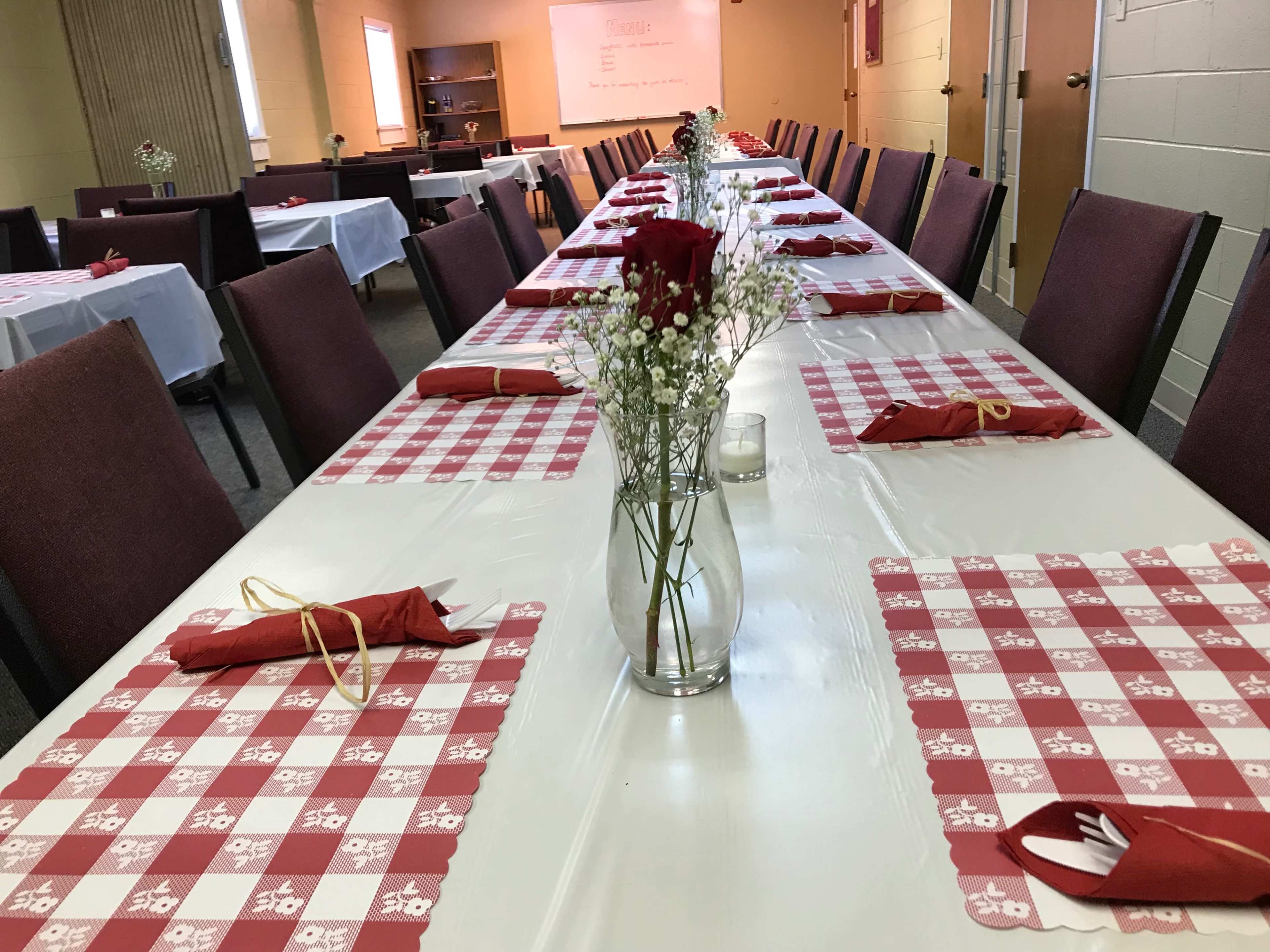 A long table is set up with red and white checked tablecloths, each adorned with a vase of flowers and neatly arranged napkins.
