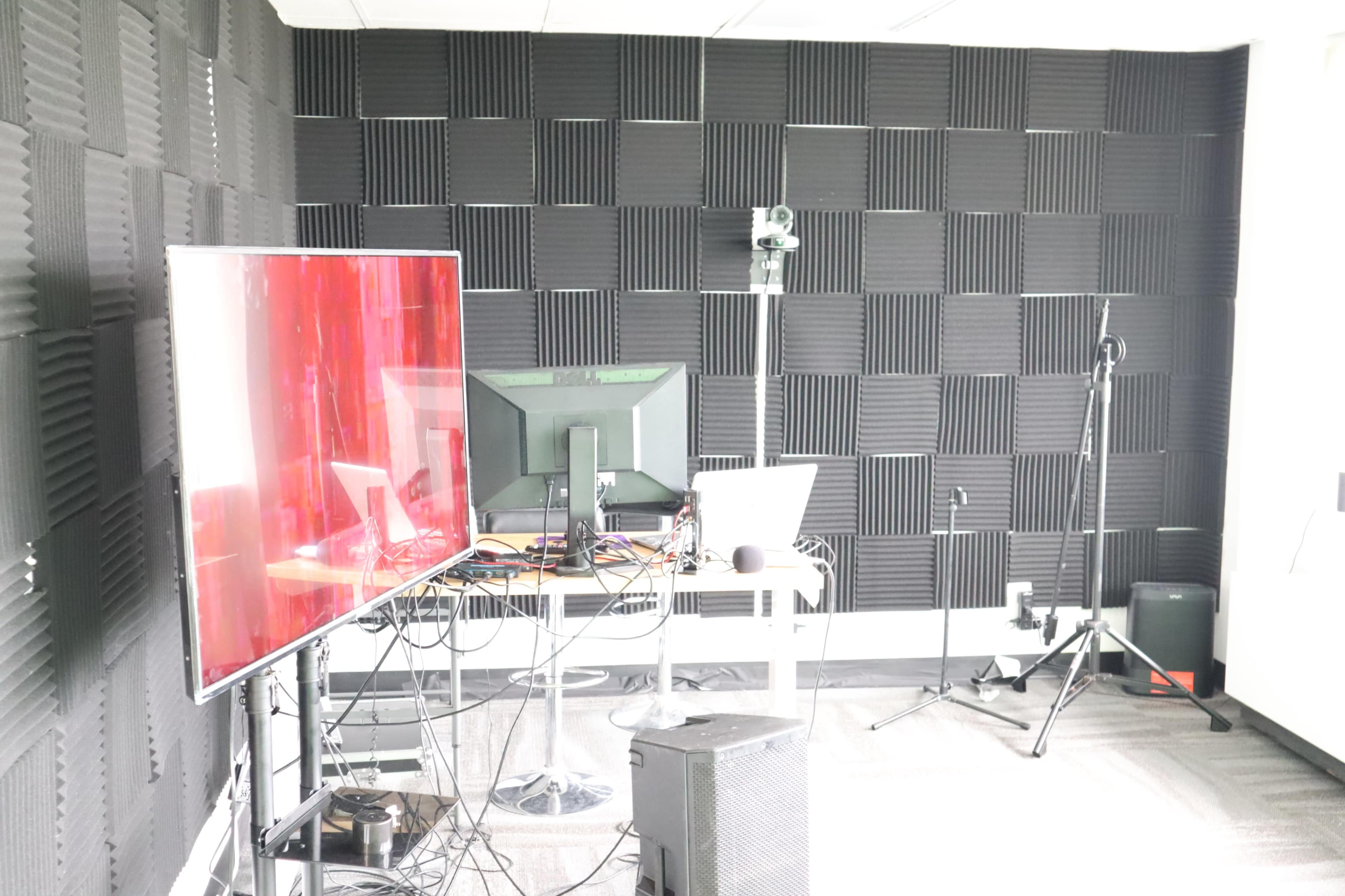 A room with soundproof wall panels, featuring a large screen, computer monitors, and various cables on a table.
