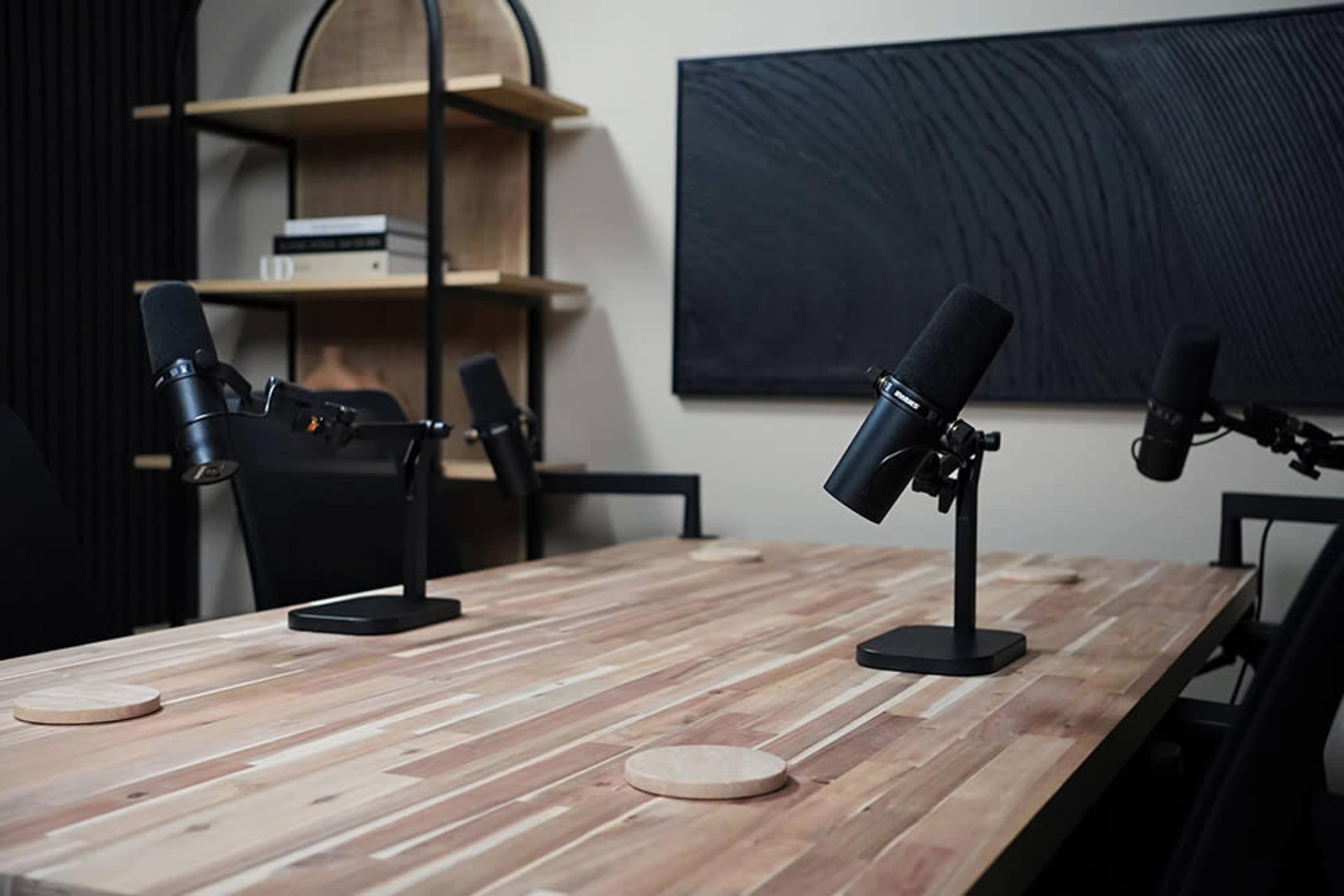 A wooden conference table with four black microphones mounted on stands is set up in a modern meeting room.