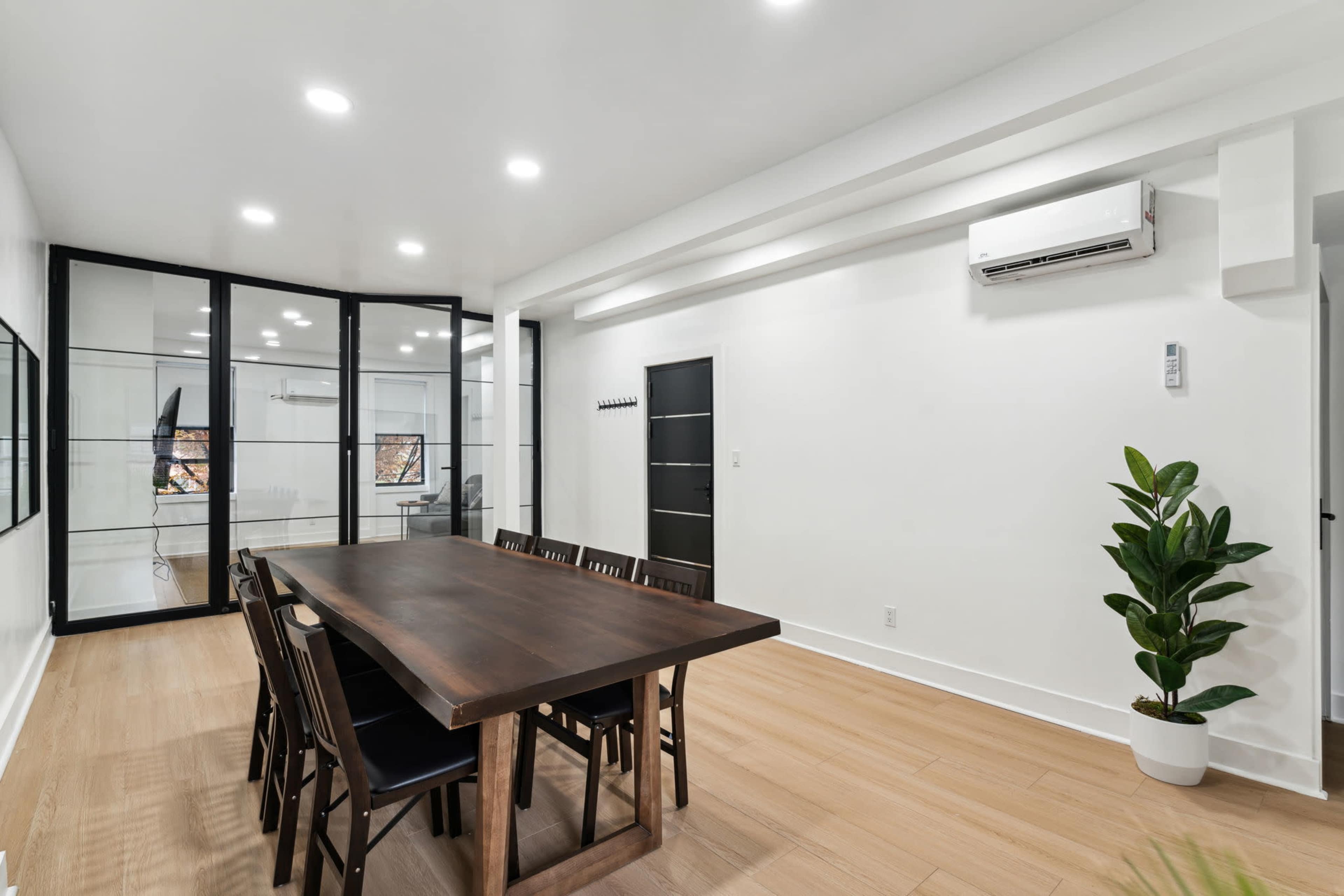 A modern meeting room features a large wooden table surrounded by chairs, with glass partitions and an air conditioning unit on the wall.