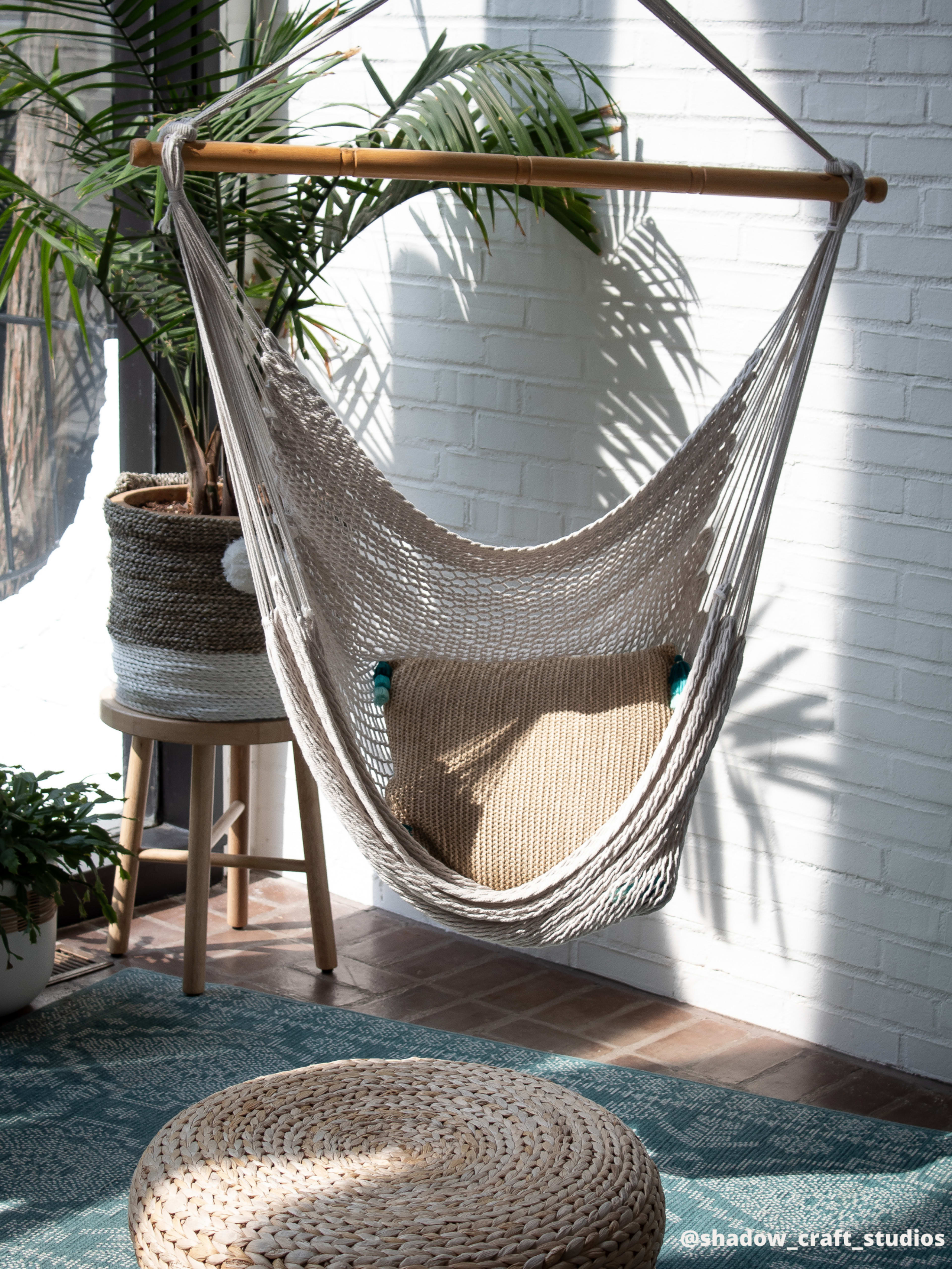 A hanging macramé hammock is suspended in a well-lit indoor space adorned with greenery and natural décor.
