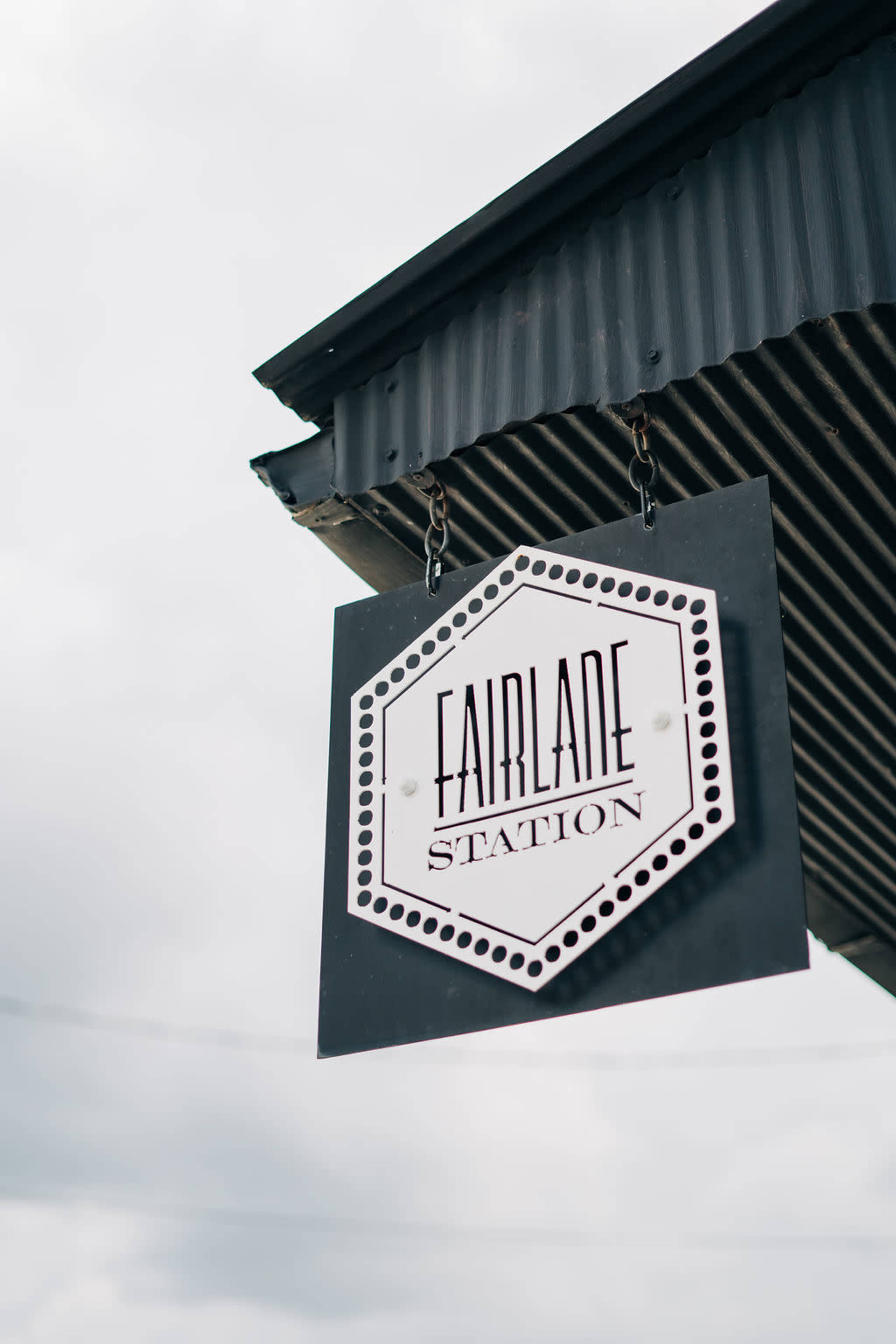 A sign that reads "Fairlade Station" hanging from a building.