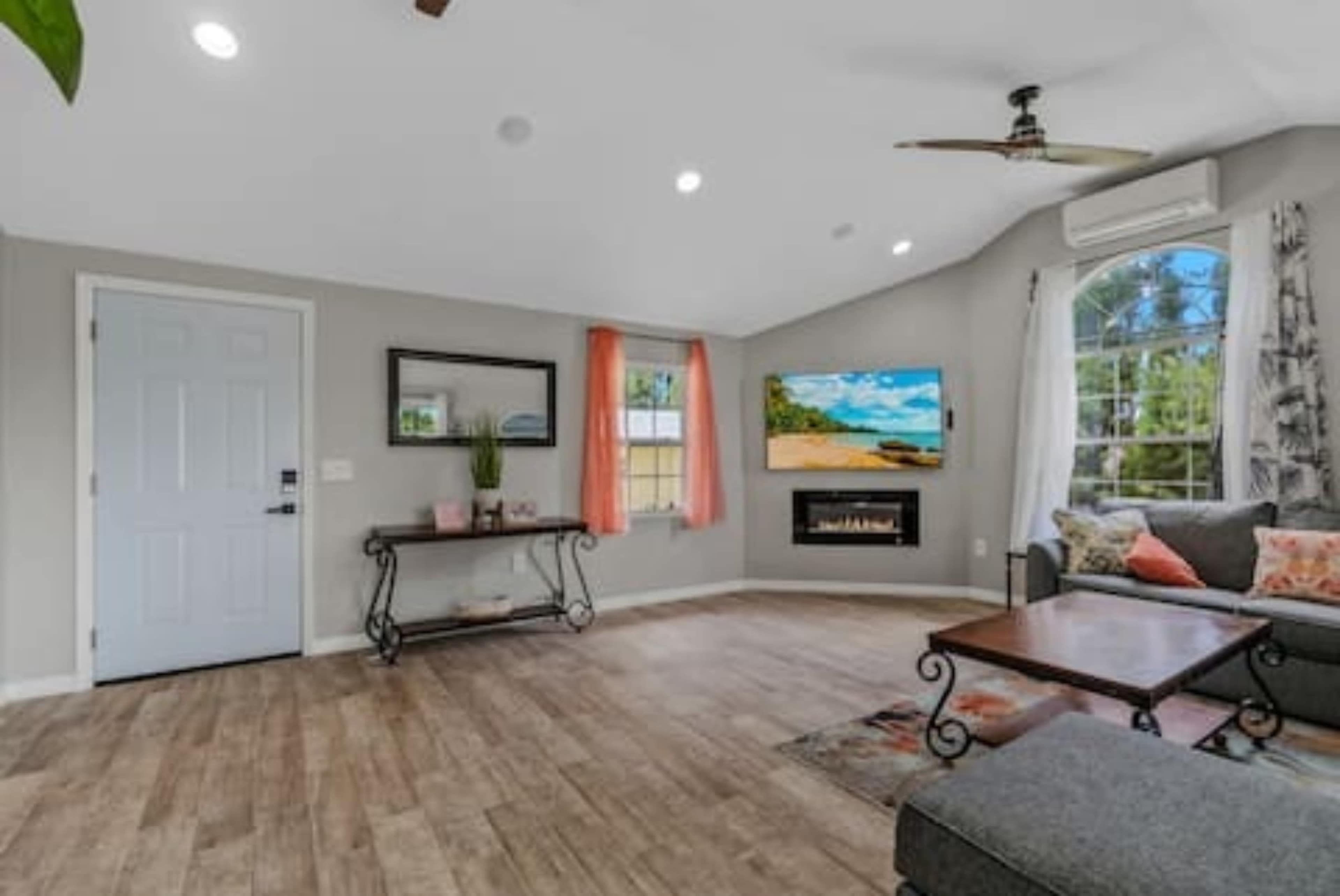 The living room features a TV mounted on the wall above an electric fireplace, accompanied by a sofa, coffee table, and a front door with a decorative console table.