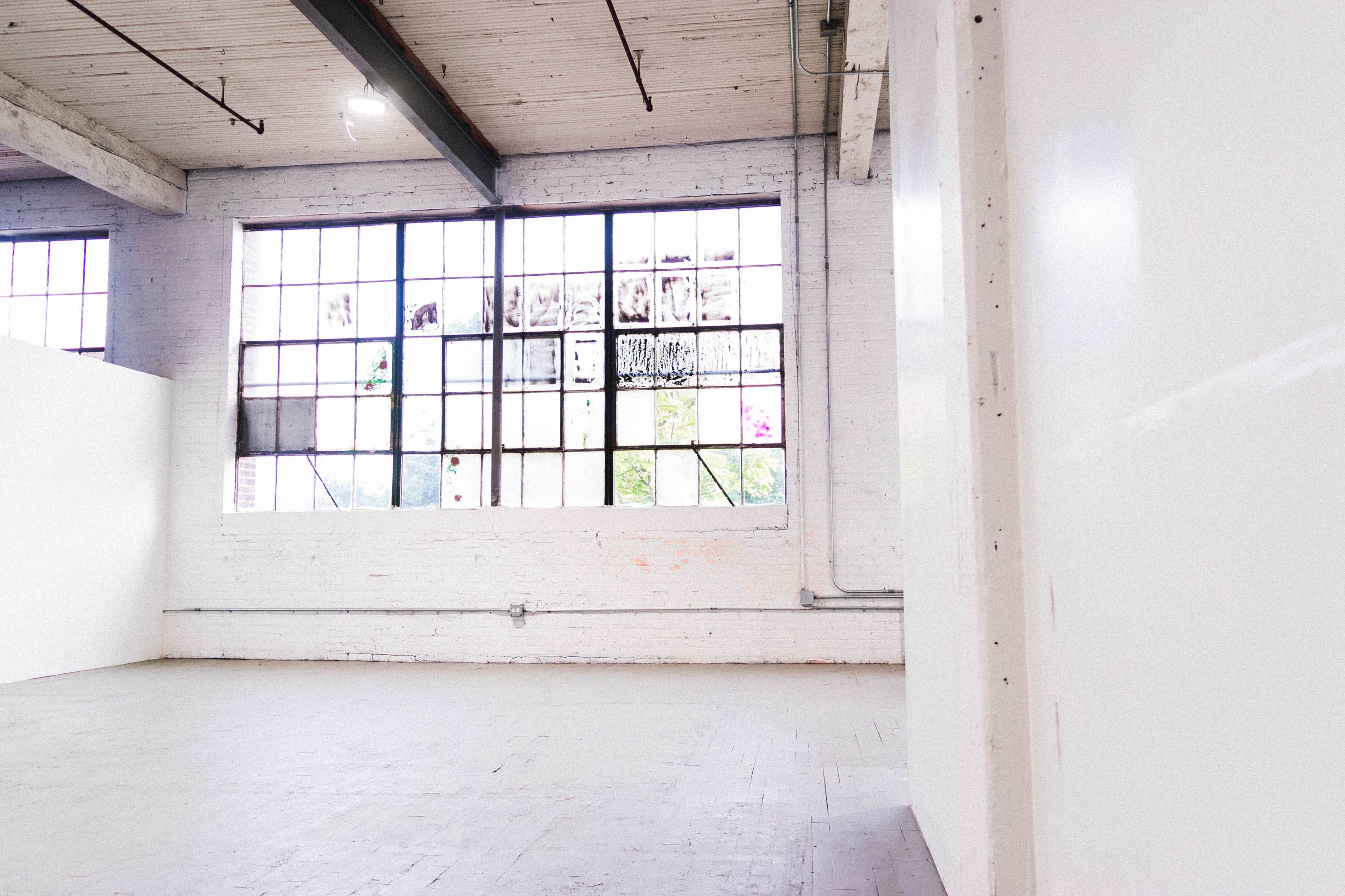 The image shows a spacious, well-lit interior with large windows and bare walls.